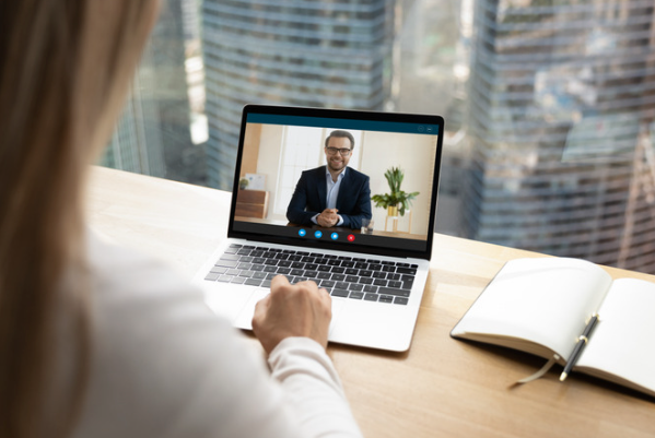 Professional conducting a virtual business meeting on laptop in modern office setting with city skyline view.