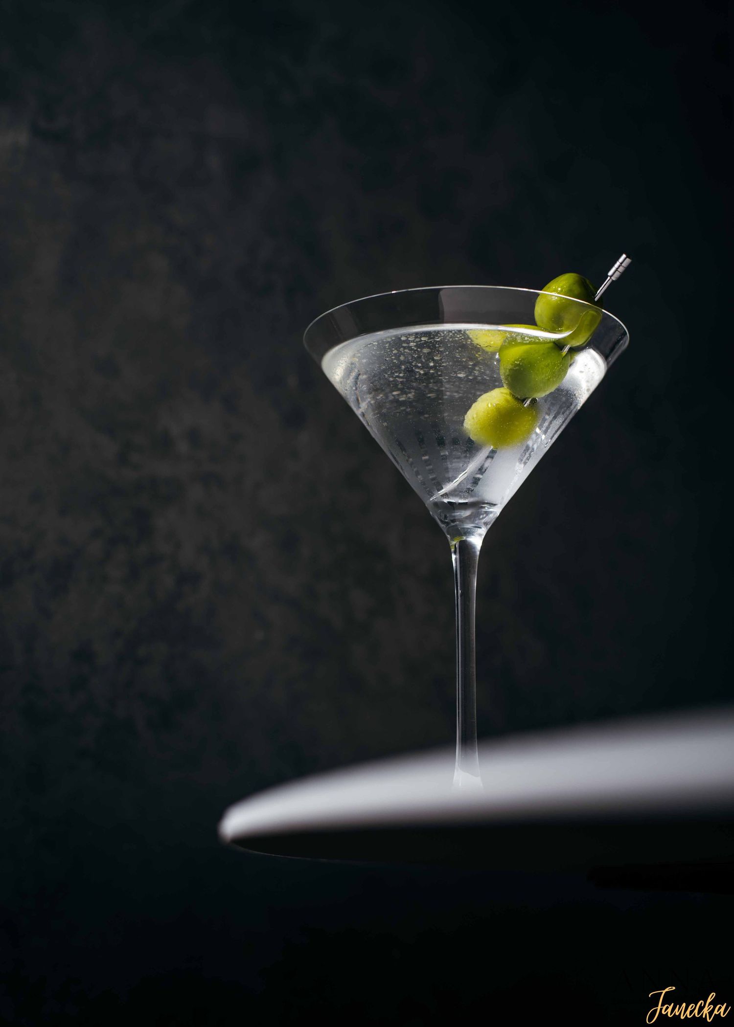 A martini glass with olive garnish against dark background shown in progressive sequence.