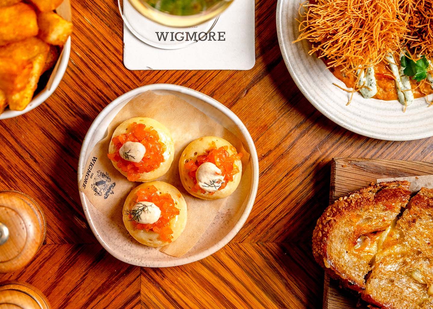 Overhead view of Wigmore restaurant table with blinis topped with salmon roe, toasted bread, and crispy garnished dishes.