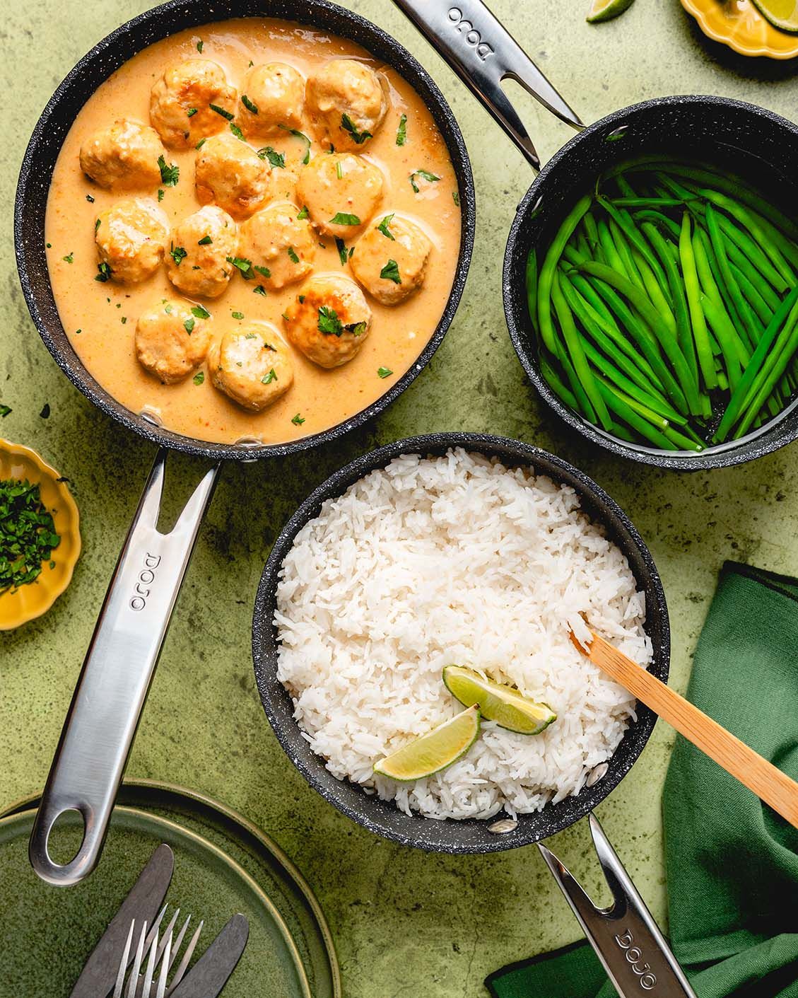Thai curry meatballs in creamy sauce served with steamed white rice and green beans in dark cookware.