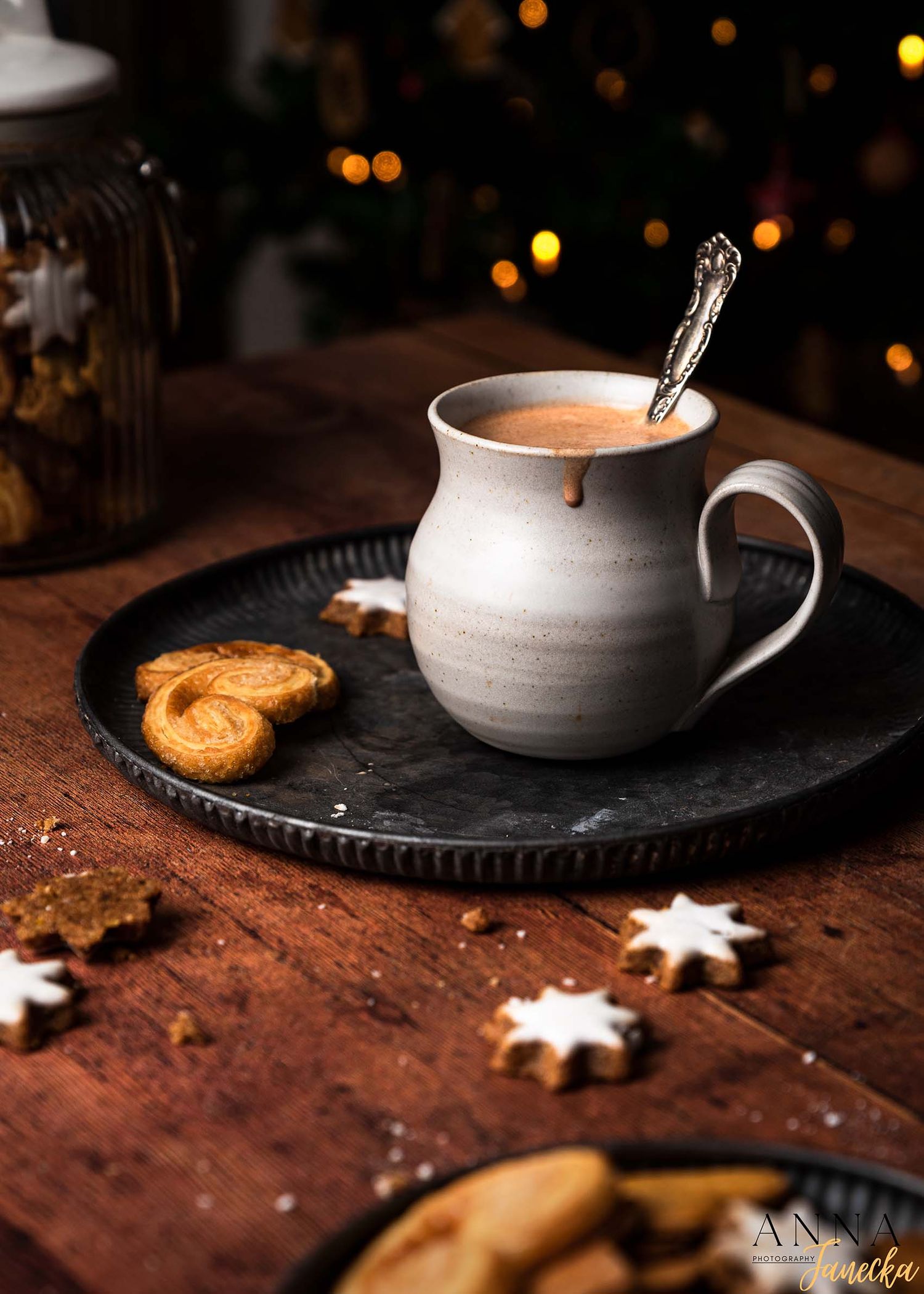 White ceramic coffee cup with cookie on dark rustic wooden table with cozy lighting.