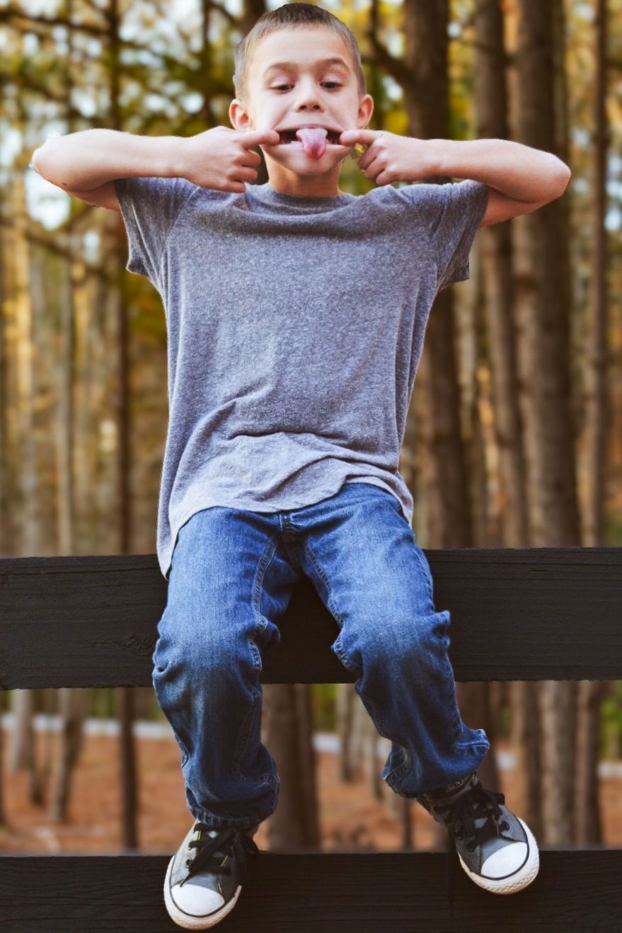 Child sitting on dark bench wearing grey shirt and jeans in forest setting.
