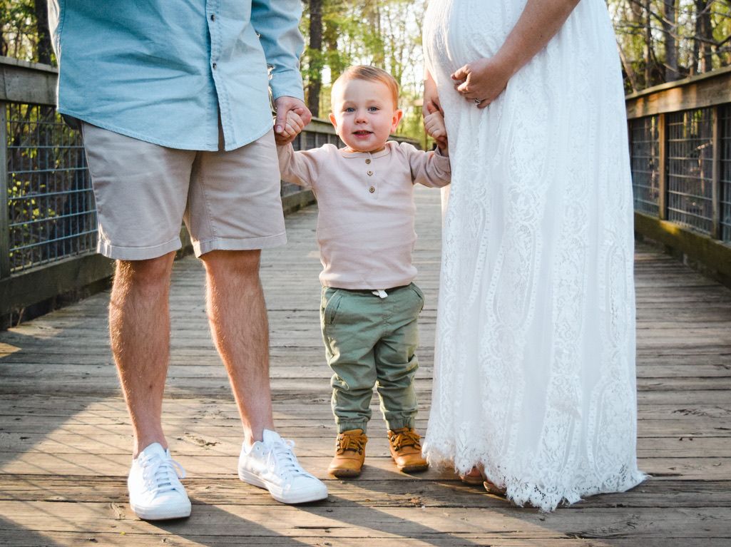 Small toddler standing between parents on wooden bridge wearing casual clothes.
