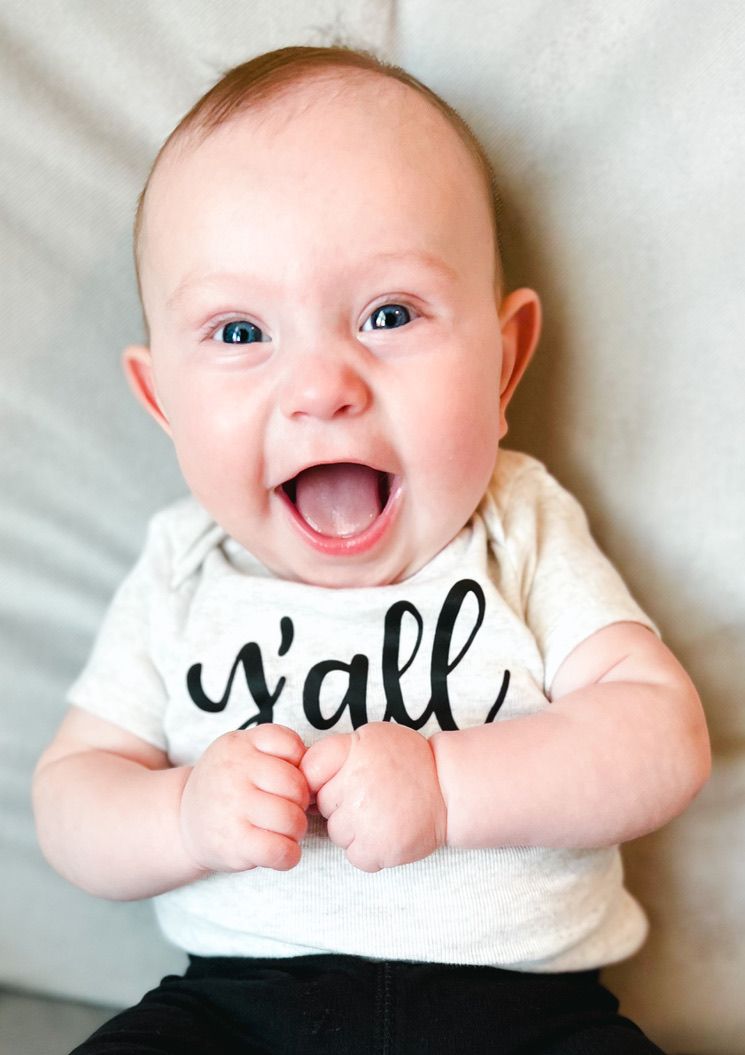Happy baby lying on white bedding showing joyful expressions and bright smiles.