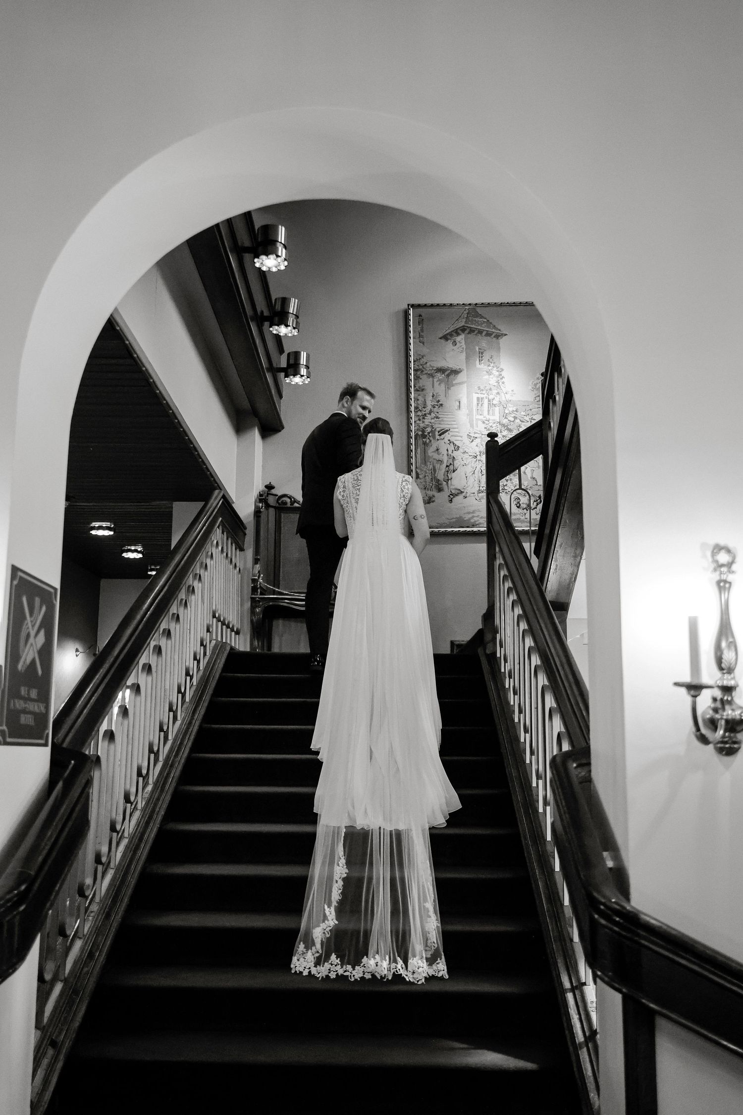 Bride and groom walking up elegant staircase in black and white wedding photo.