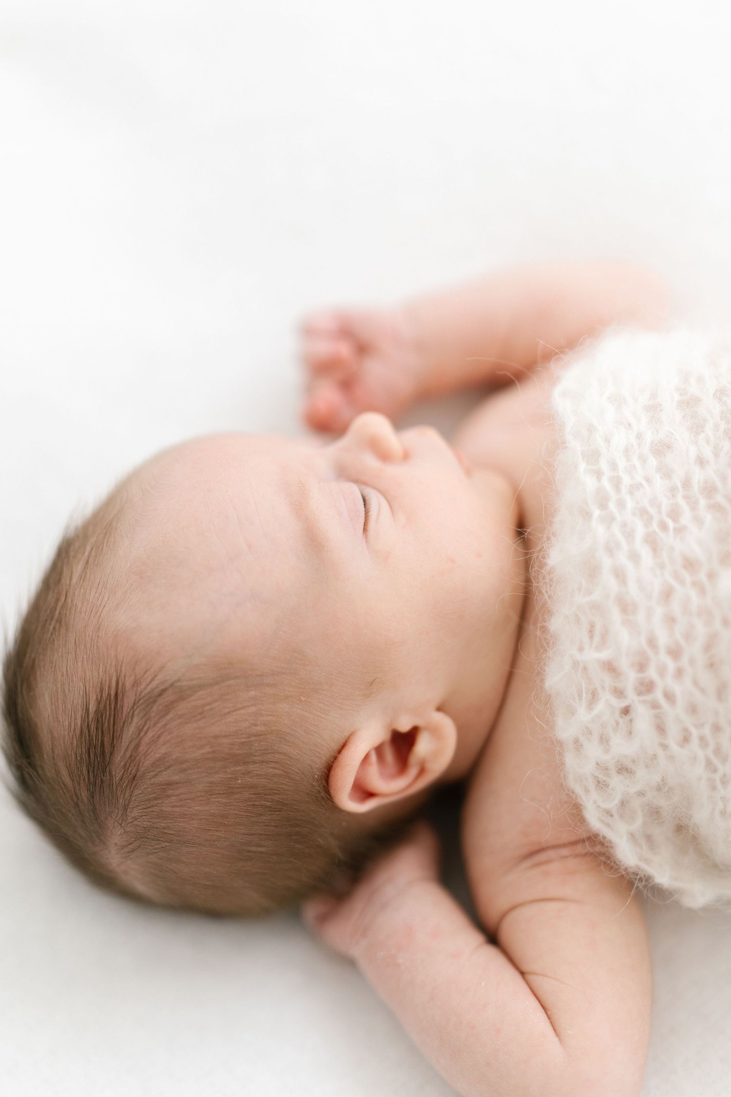 A sleeping baby lies peacefully on white lace fabric in a minimalist newborn portrait.