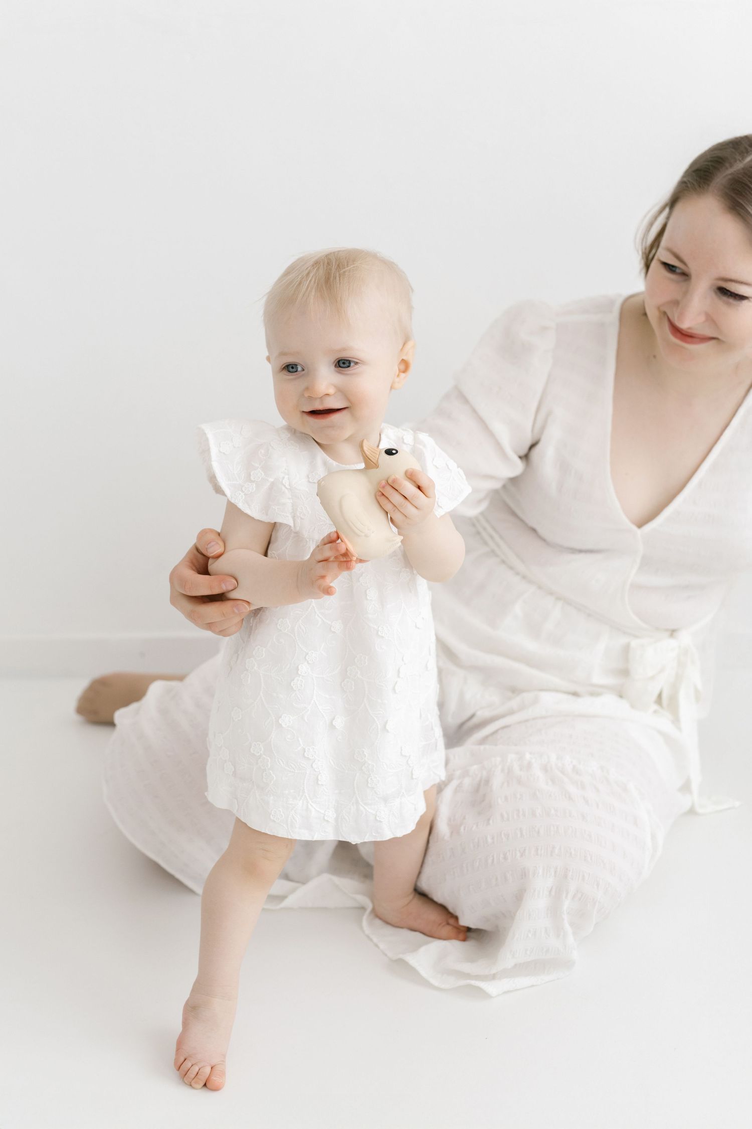 A tender moment captured in white clothing against a minimalist light background.