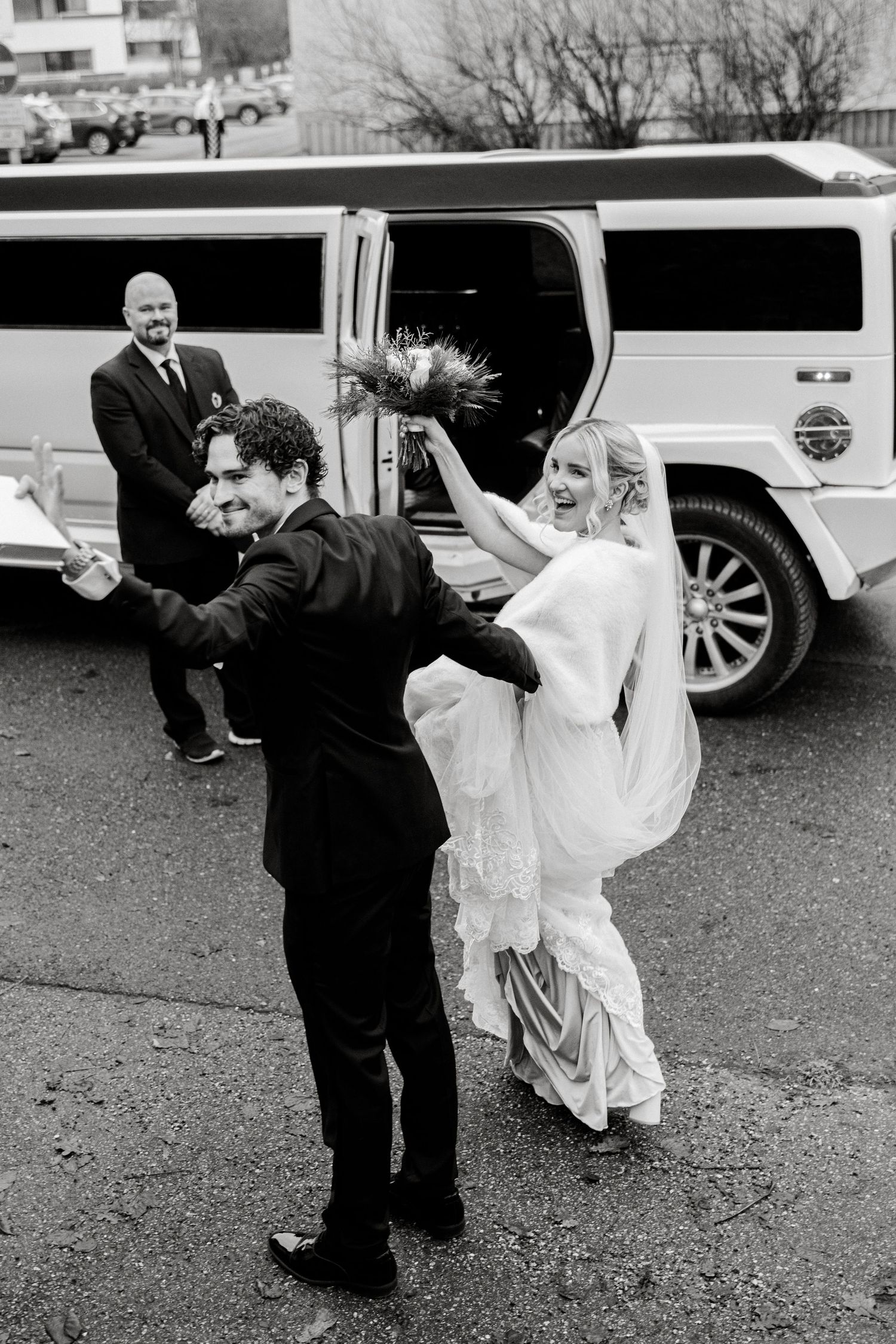 Playful black and white photo of newlyweds dancing in parking lot after wedding ceremony.