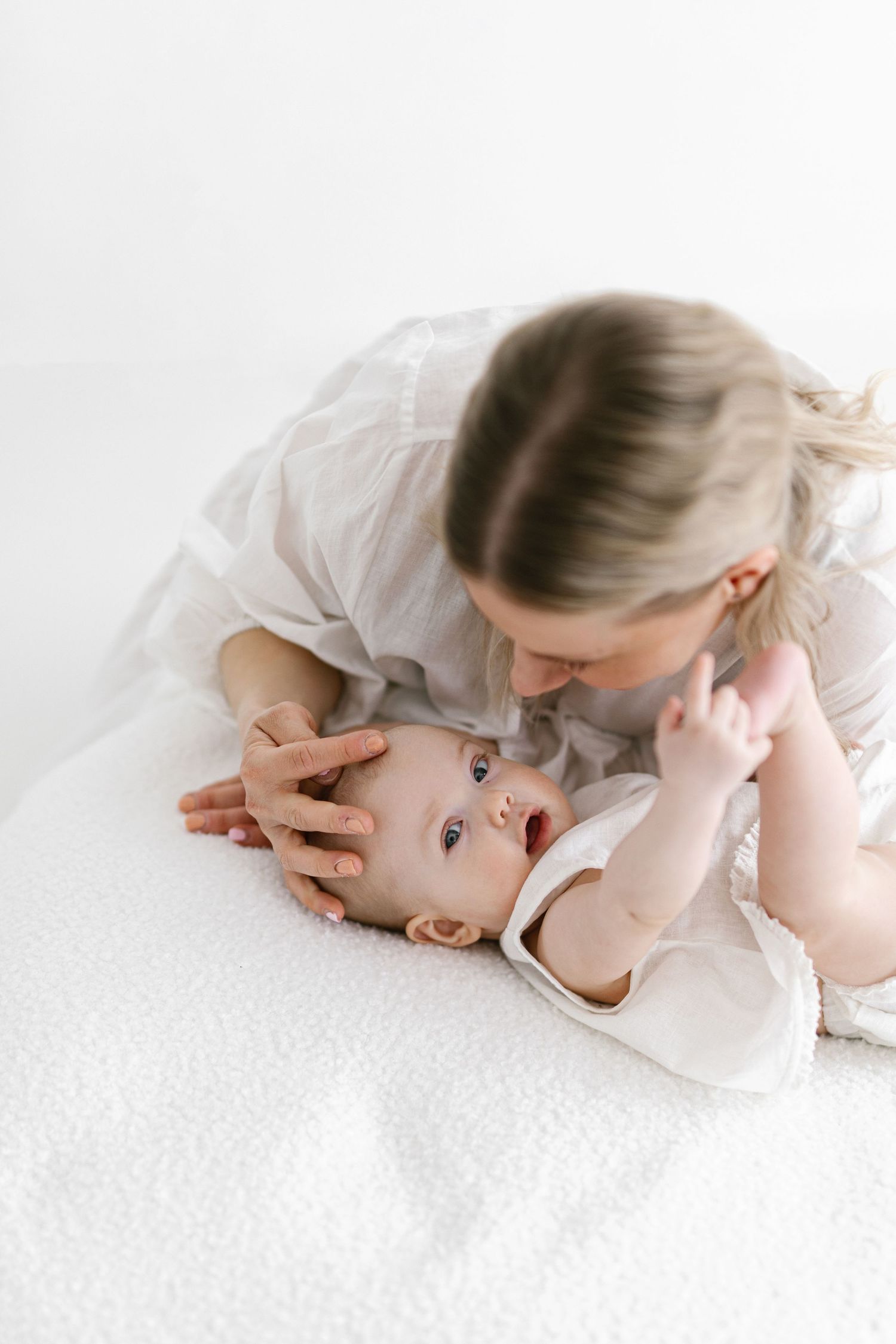 A mother tenderly cradles her newborn baby on a white blanket in a bright, minimalist setting.
