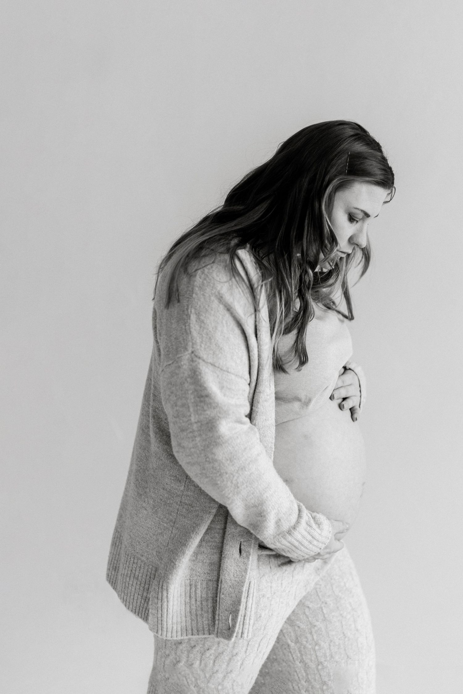 Black and white profile of an expectant mother in a cozy sweater looking down thoughtfully.