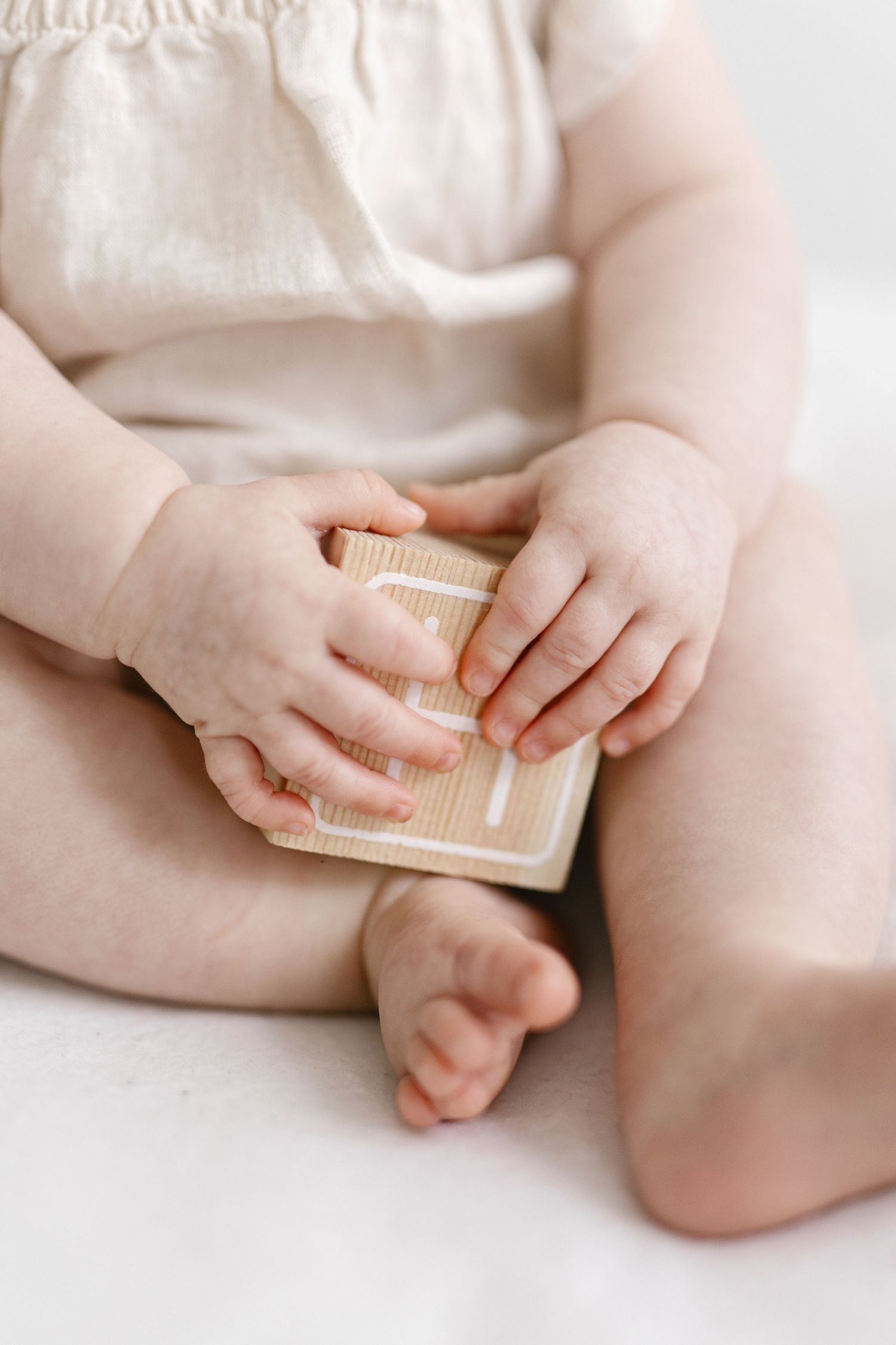 Small baby hands holding a cream-colored book while sitting on white surface.