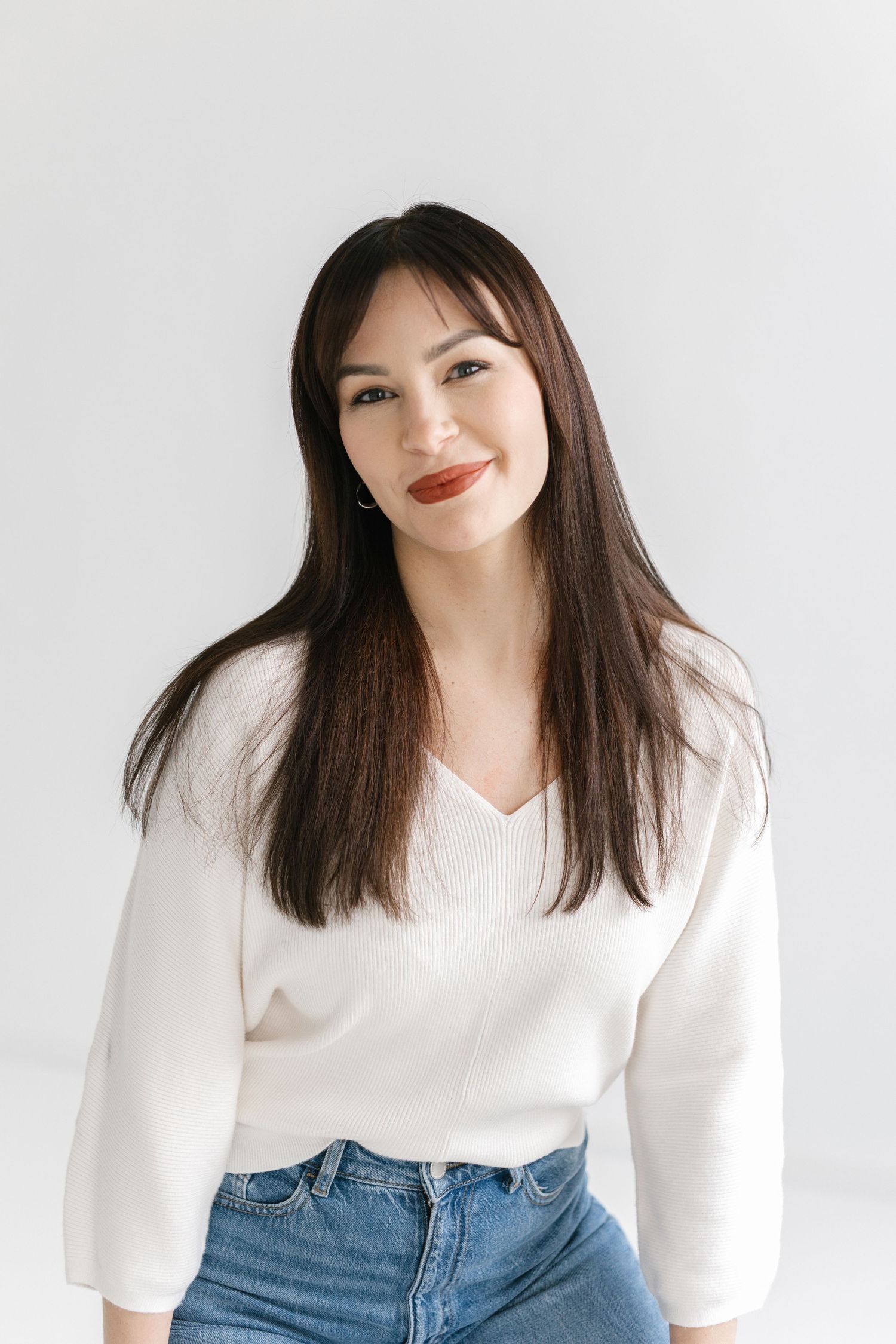 A person in a white sweater and blue jeans poses against a white background in a series of casual portrait shots.