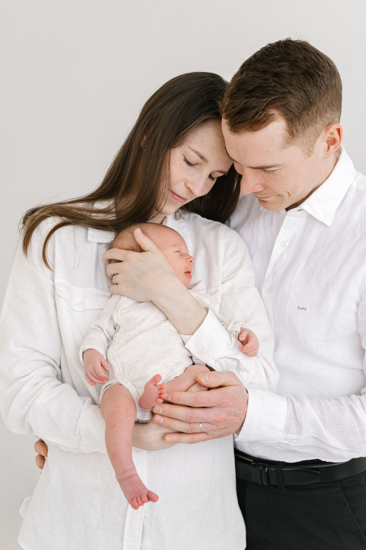 Family portrait series in white clothing showing intimate moments with their newborn baby.