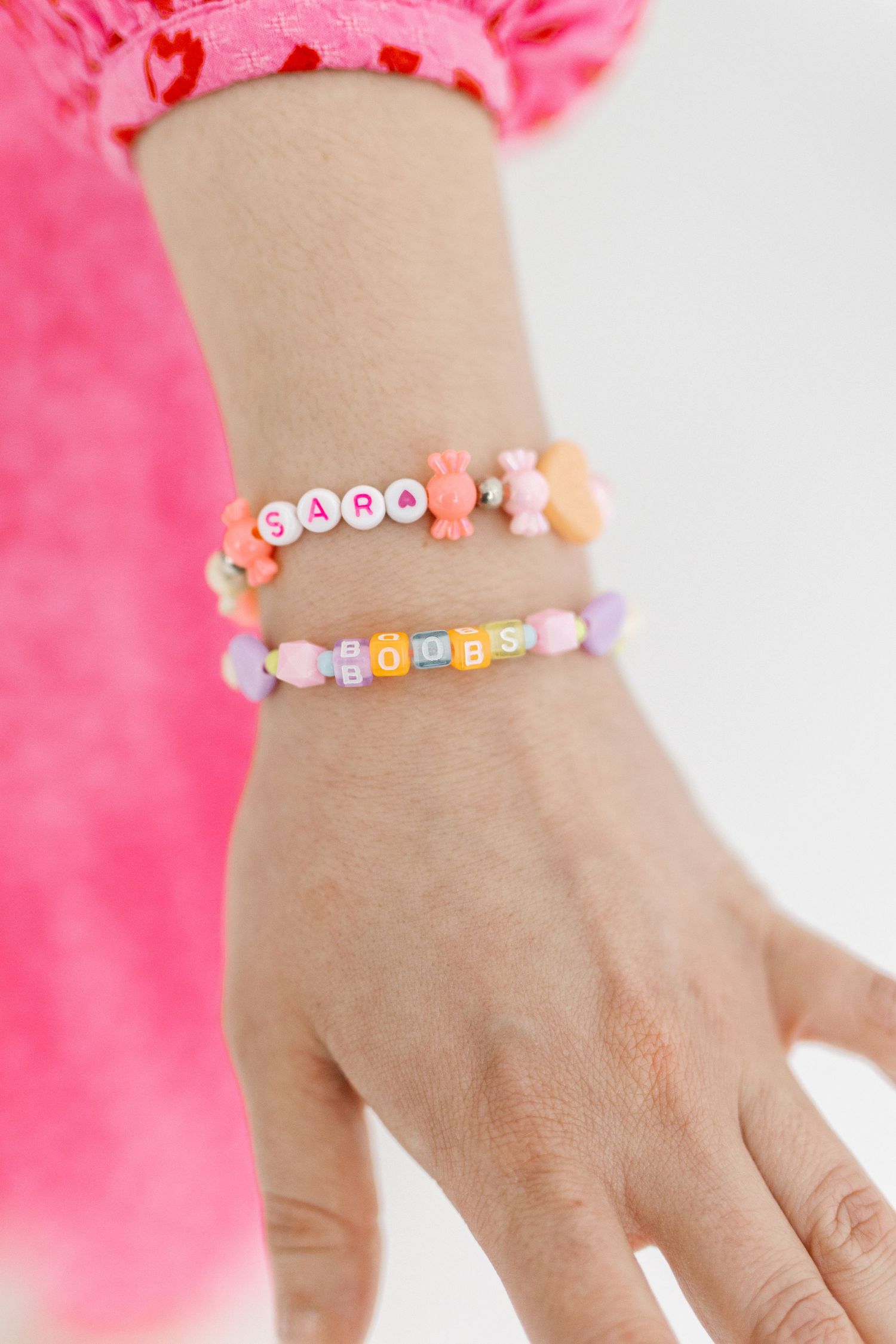 Colorful beaded friendship bracelets displayed on wrist against pink background.