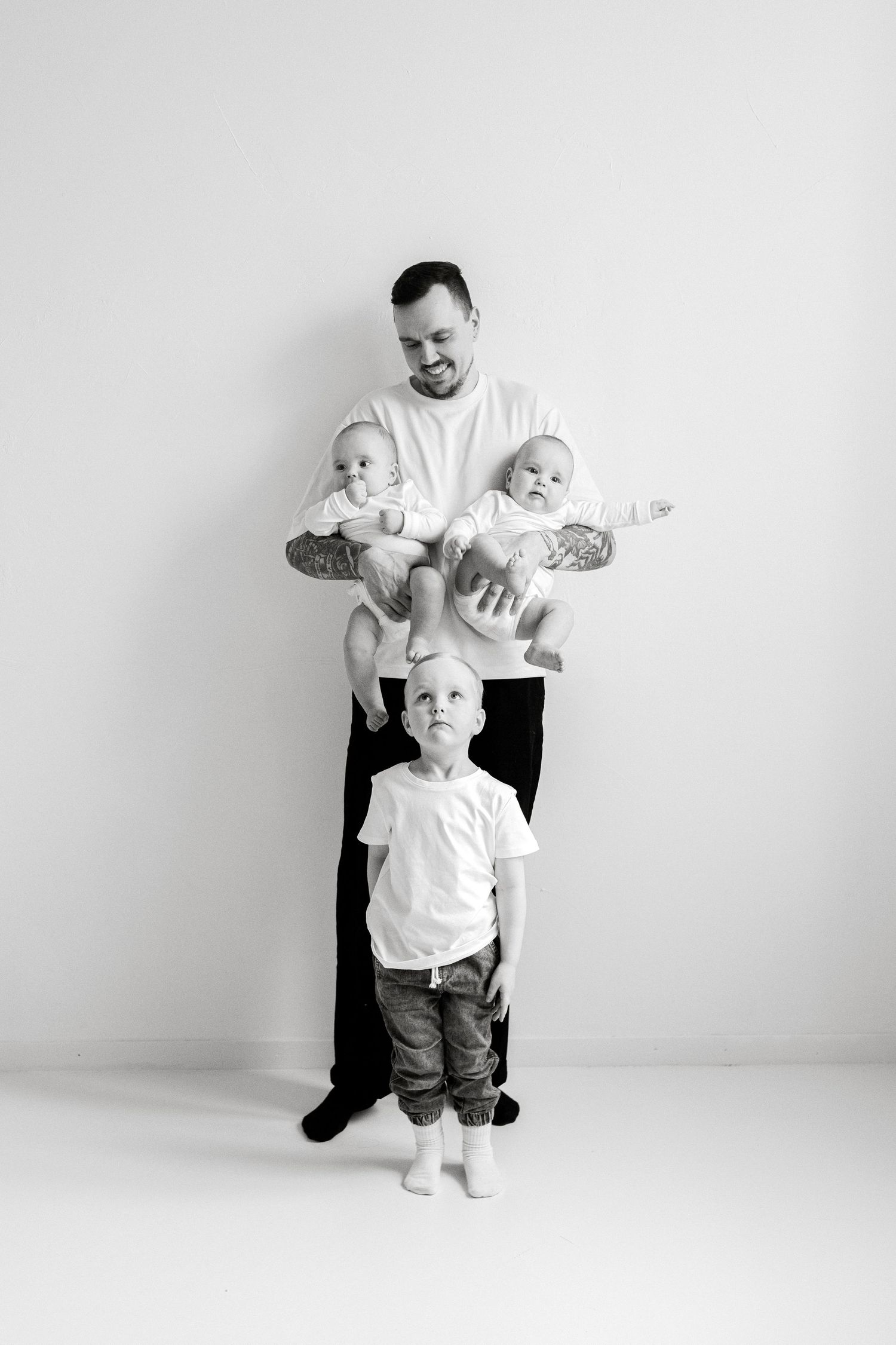 Black and white photo of a father holding twin babies while a young boy stands in front, family portrait.
