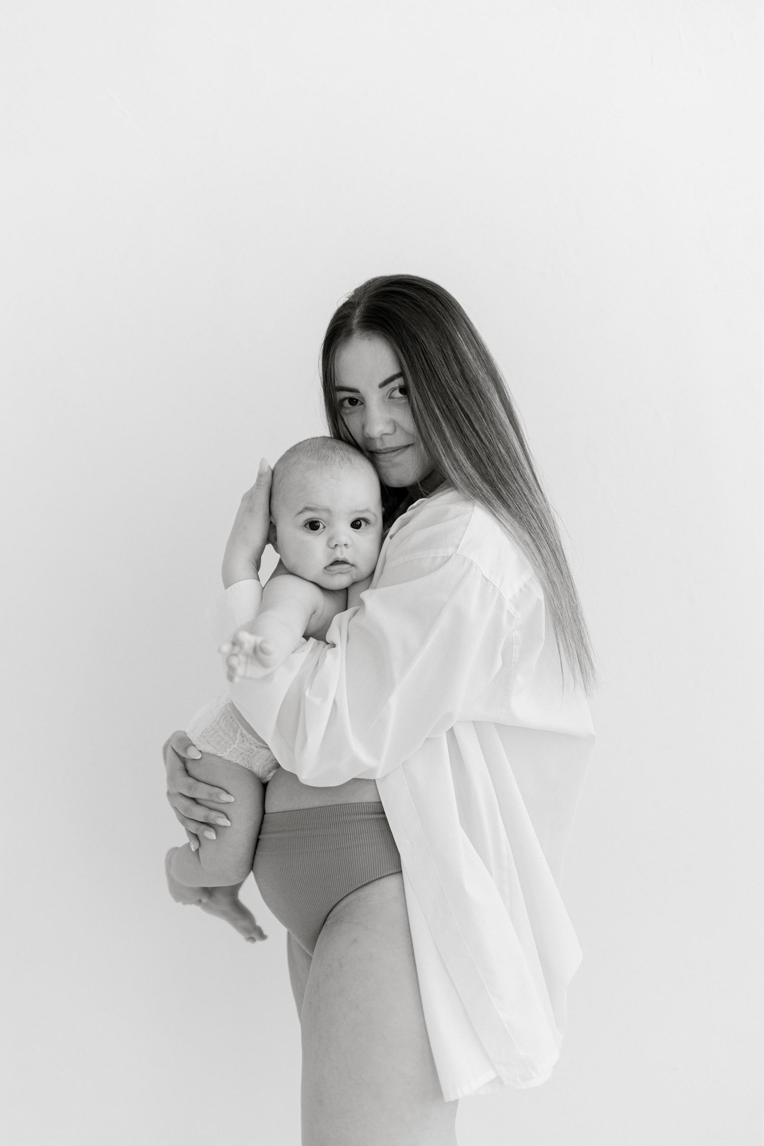 Black and white photo of a young mother tenderly holding her newborn baby against a light background.