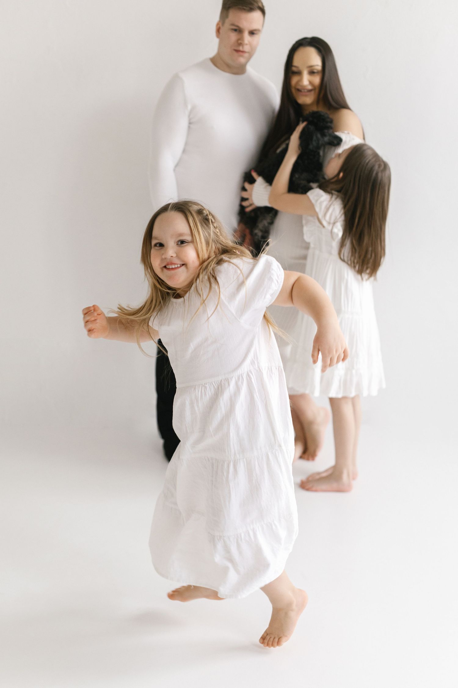 Family in white clothing playing and having fun against white backdrop.