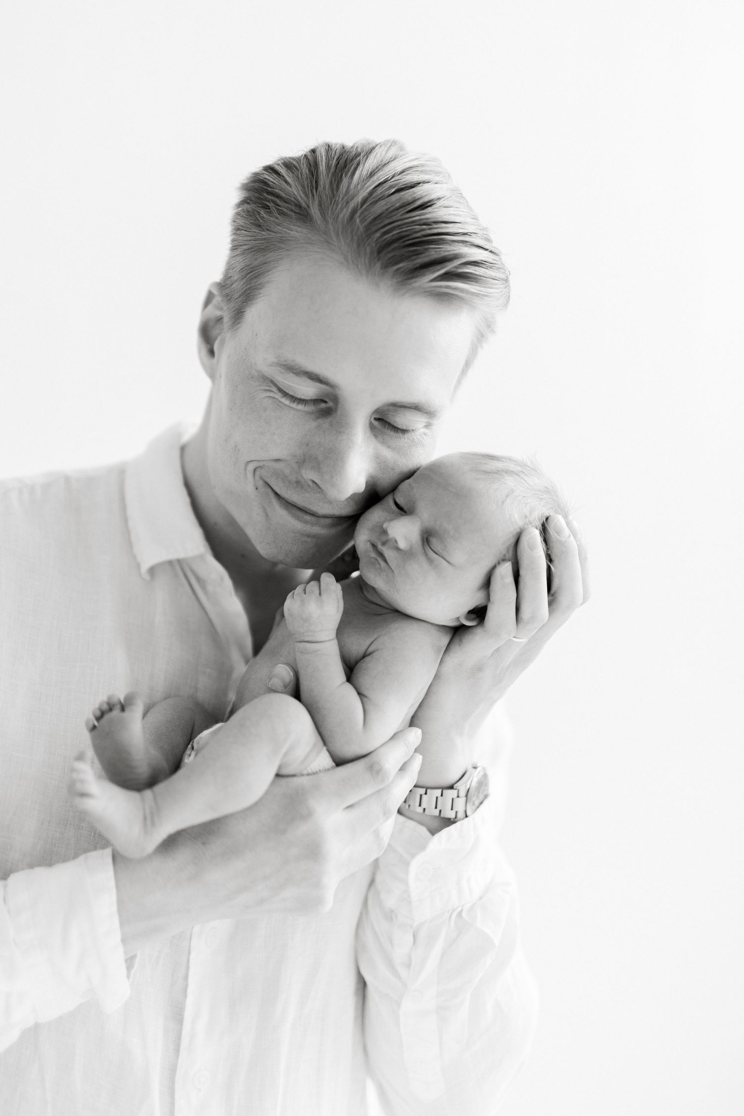 Intimate portrait of tender family moment with newborn baby against white background.