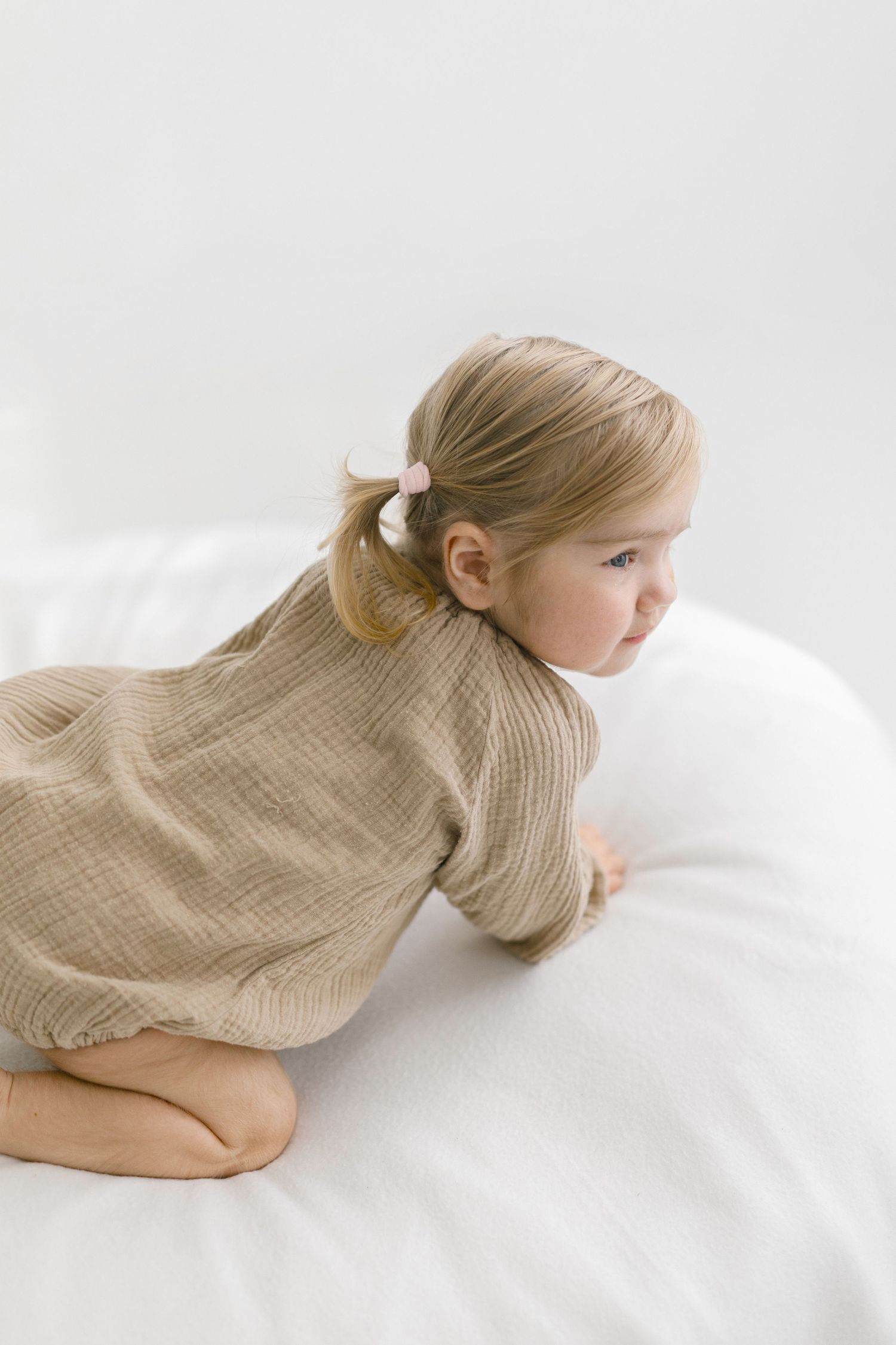 Baby in beige outfit lying on white surface during photo session.