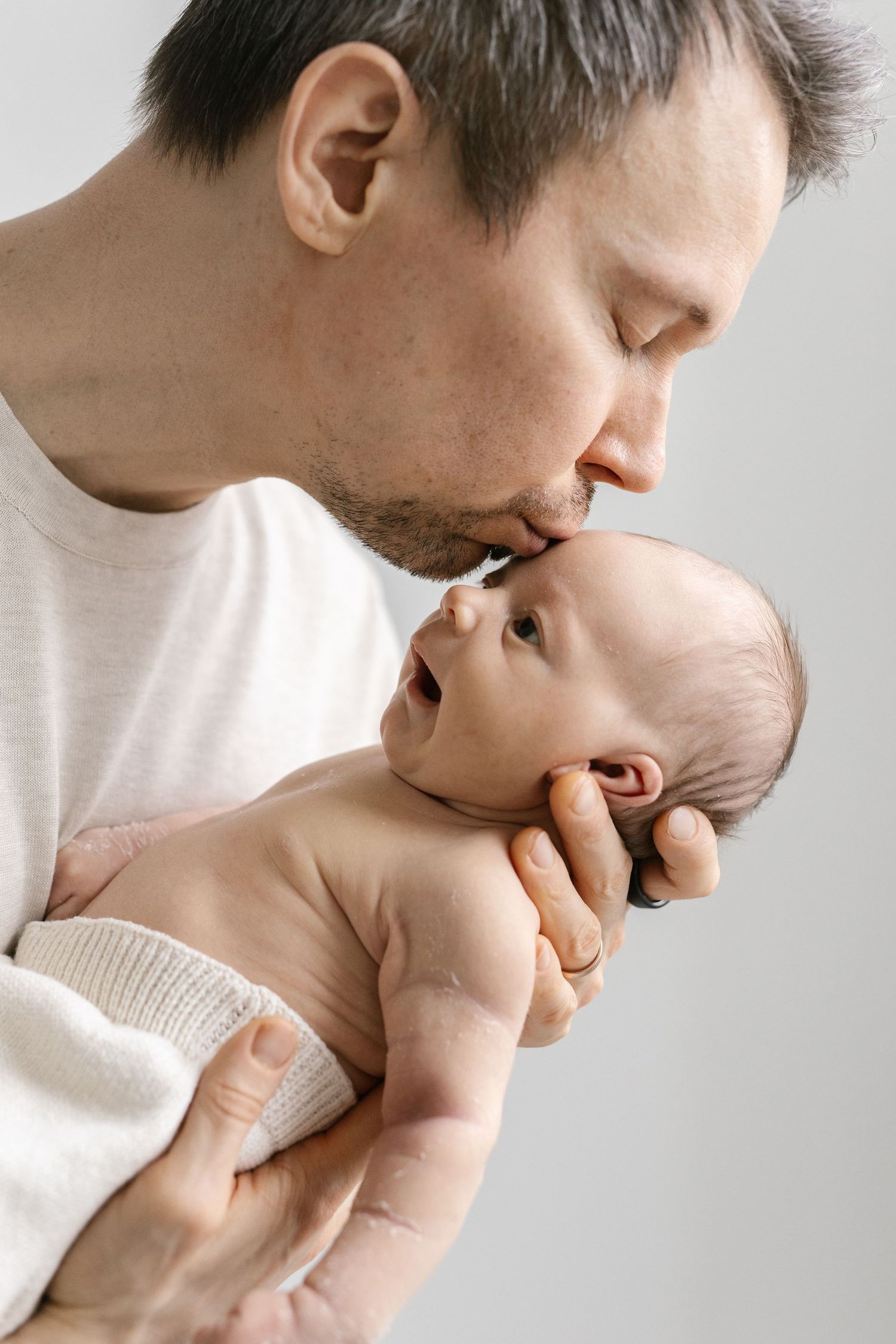 Intimate moment between parent and baby captured in profile against light background.