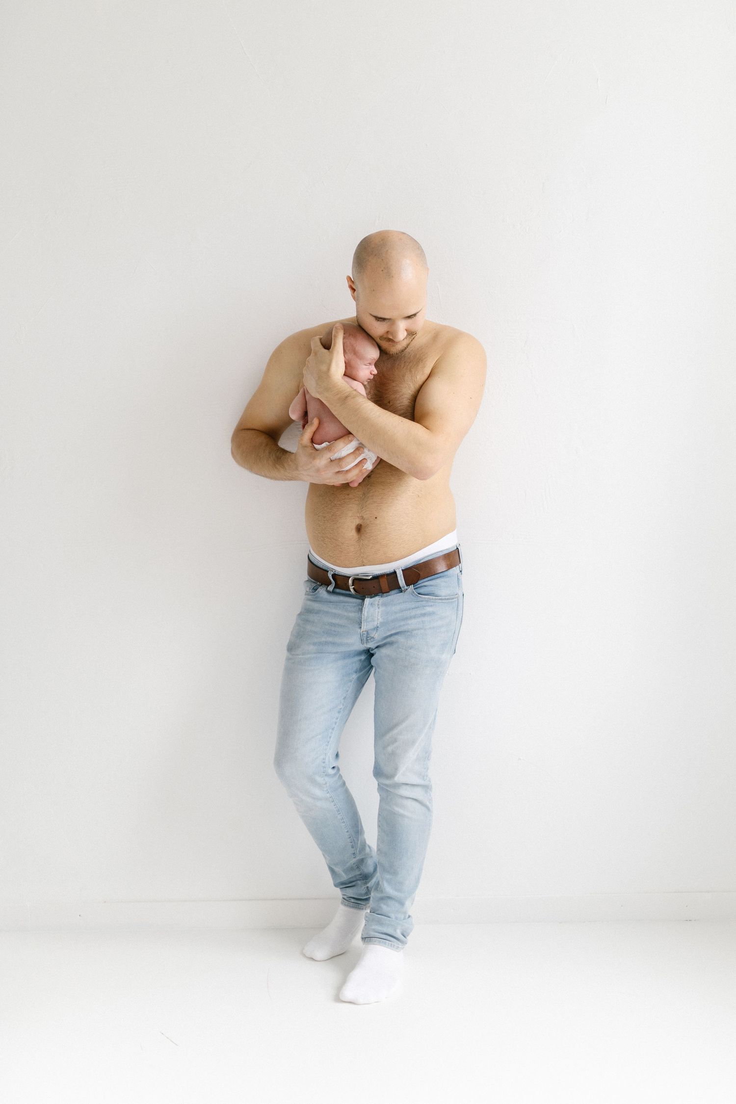 Person in light jeans poses expressively against white wall in artistic portrait series.