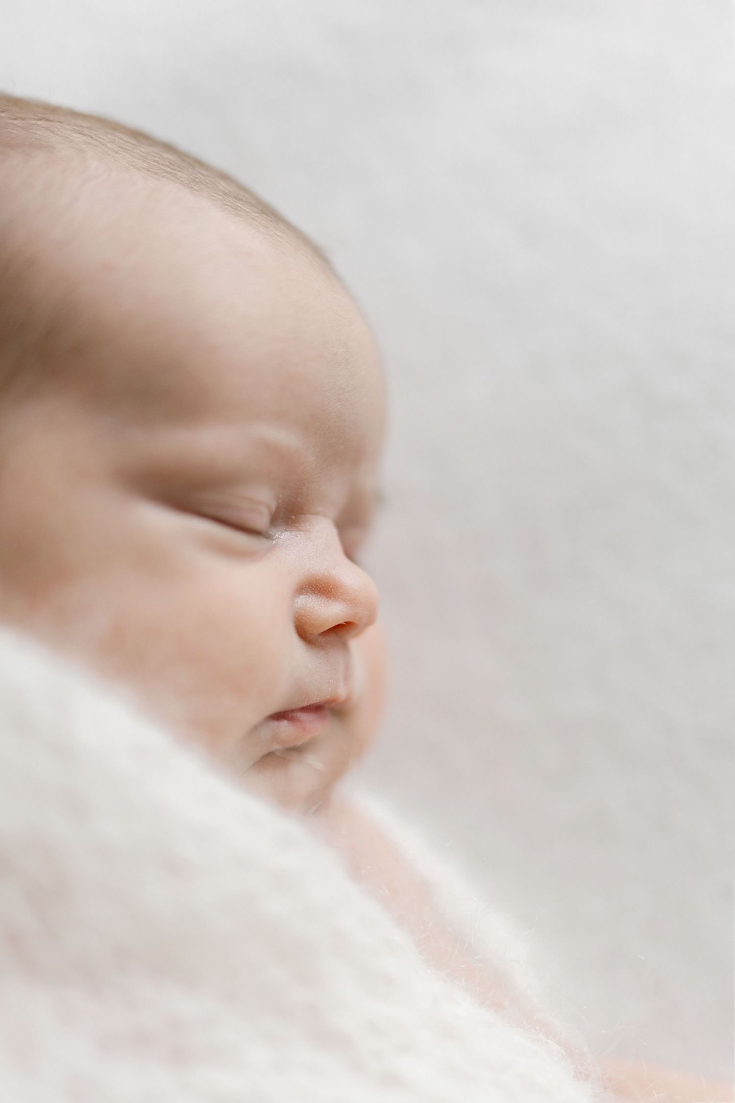 Close-up portrait of a peaceful sleeping newborn baby wrapped in a soft white blanket.