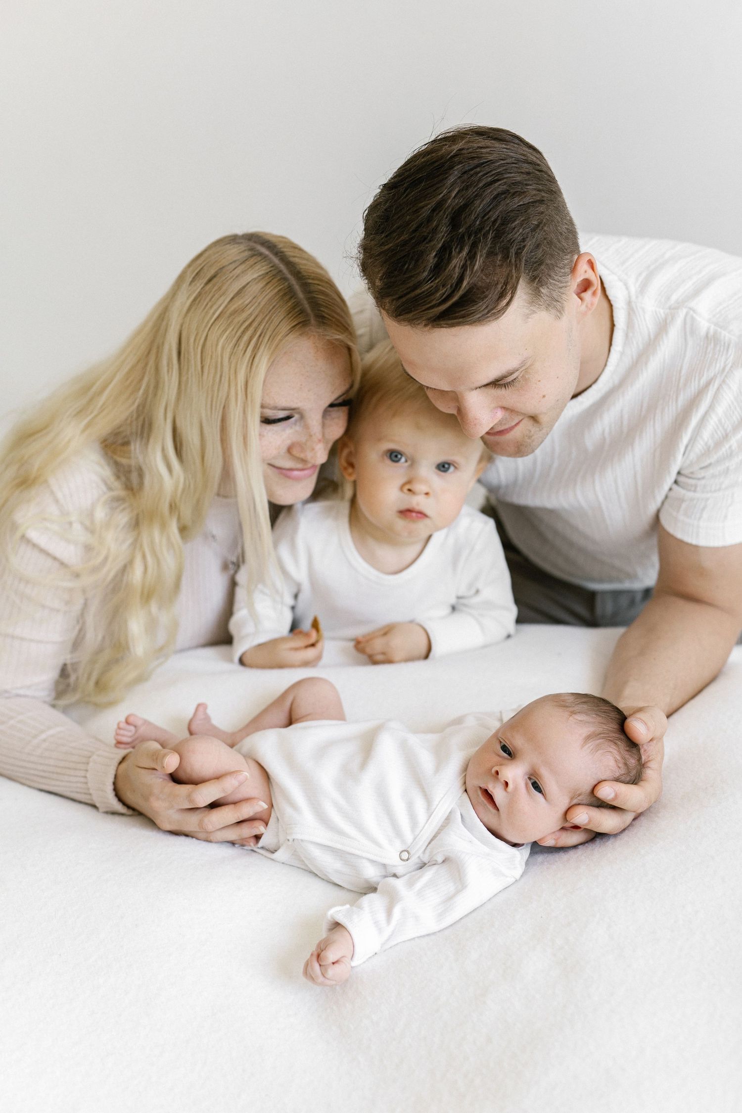 Happy family with two young children, including a newborn, posing together on a white bed in matching outfits.