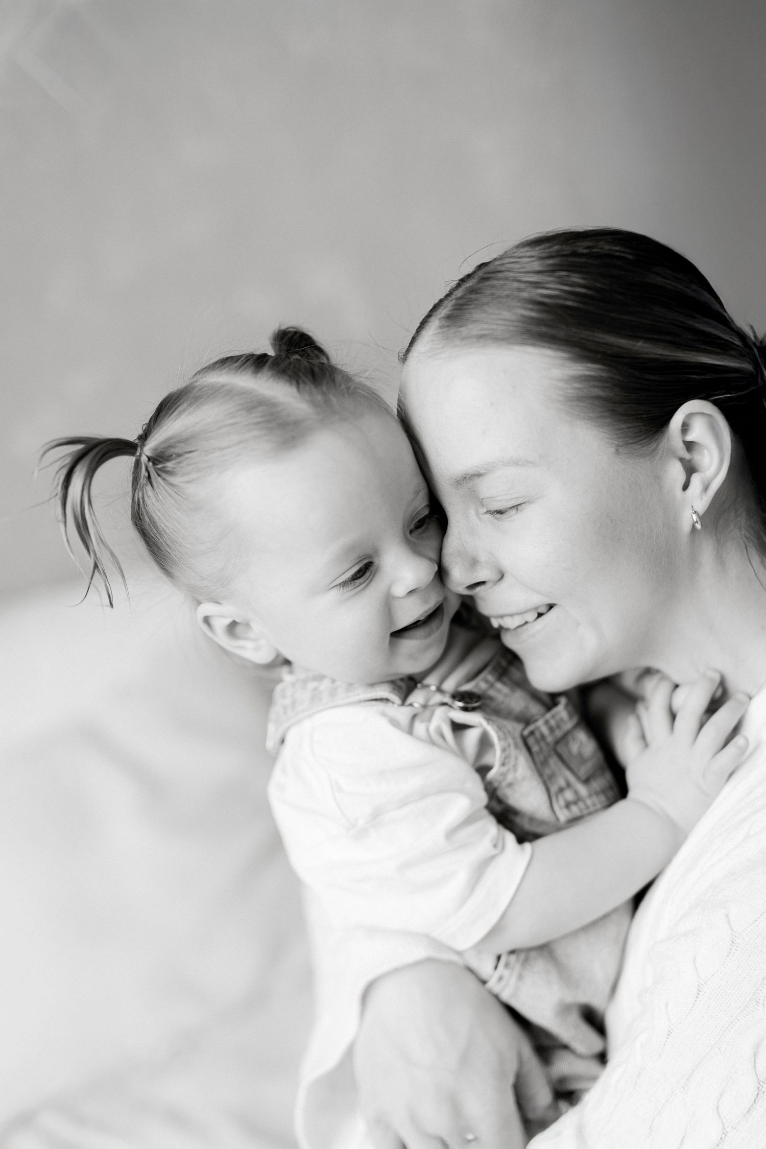 Black and white photo of a smiling mother tenderly holding her laughing toddler daughter close, sharing a joyful moment.