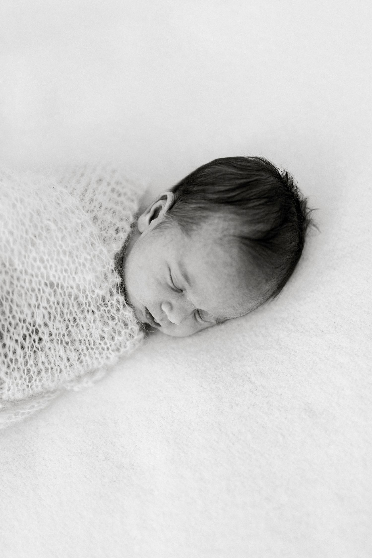 A black and white artistic portrait series shows a sleeping newborn baby nestled in soft textured fabric.