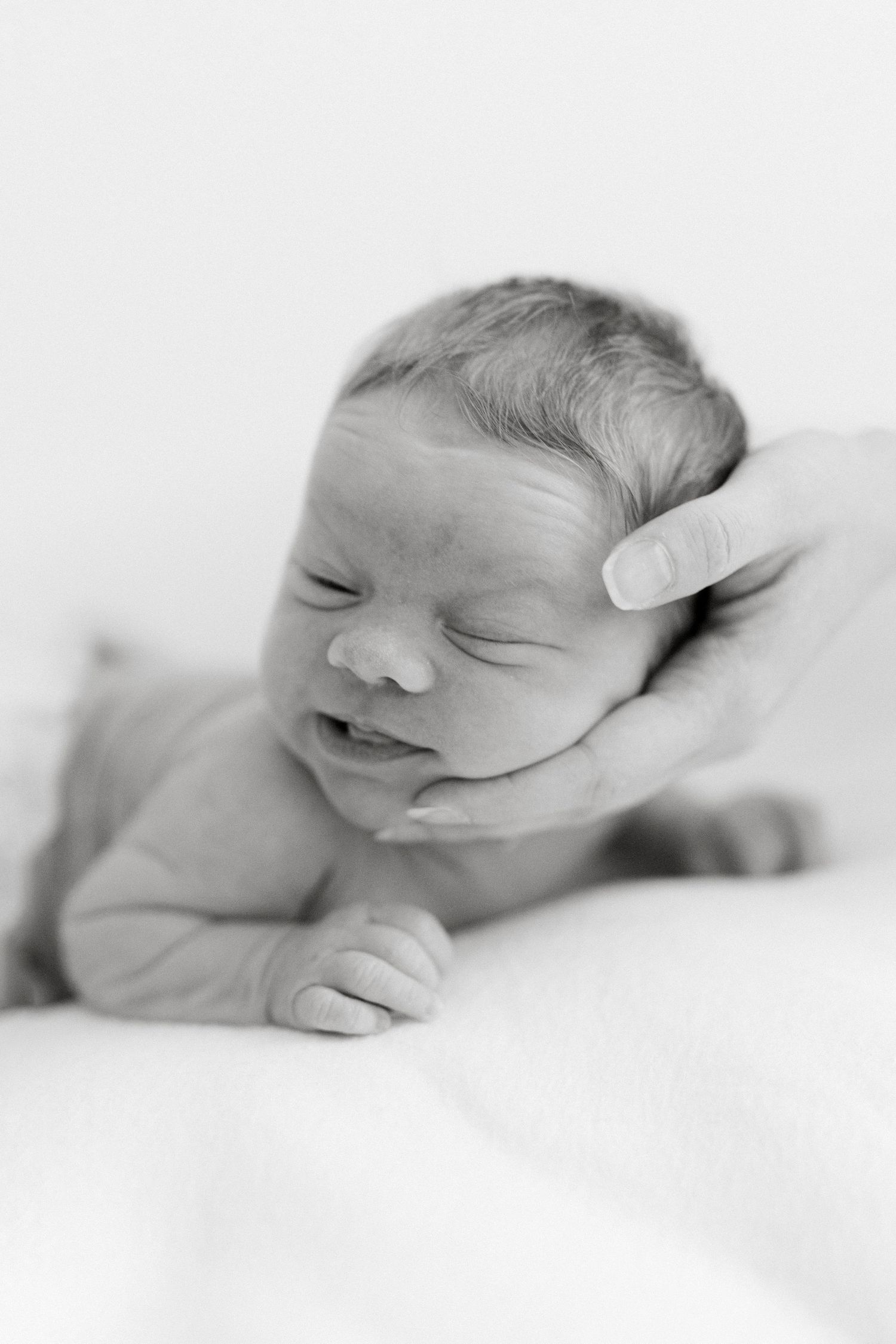 Close-up black and white portrait of a smiling newborn baby being gently cradled.