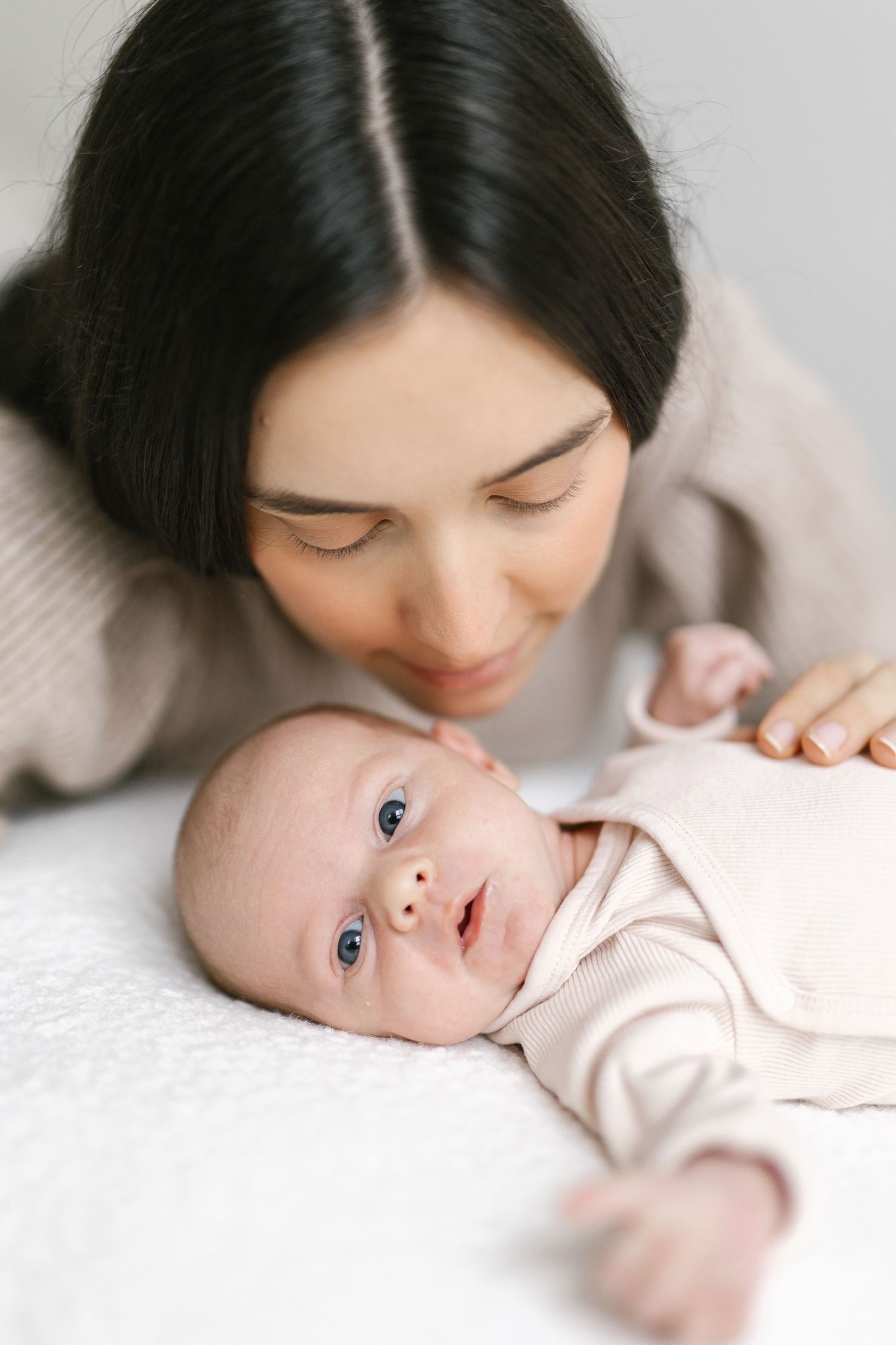 Sweet progression of a parent leaning down to kiss their baby lying on white bedding.