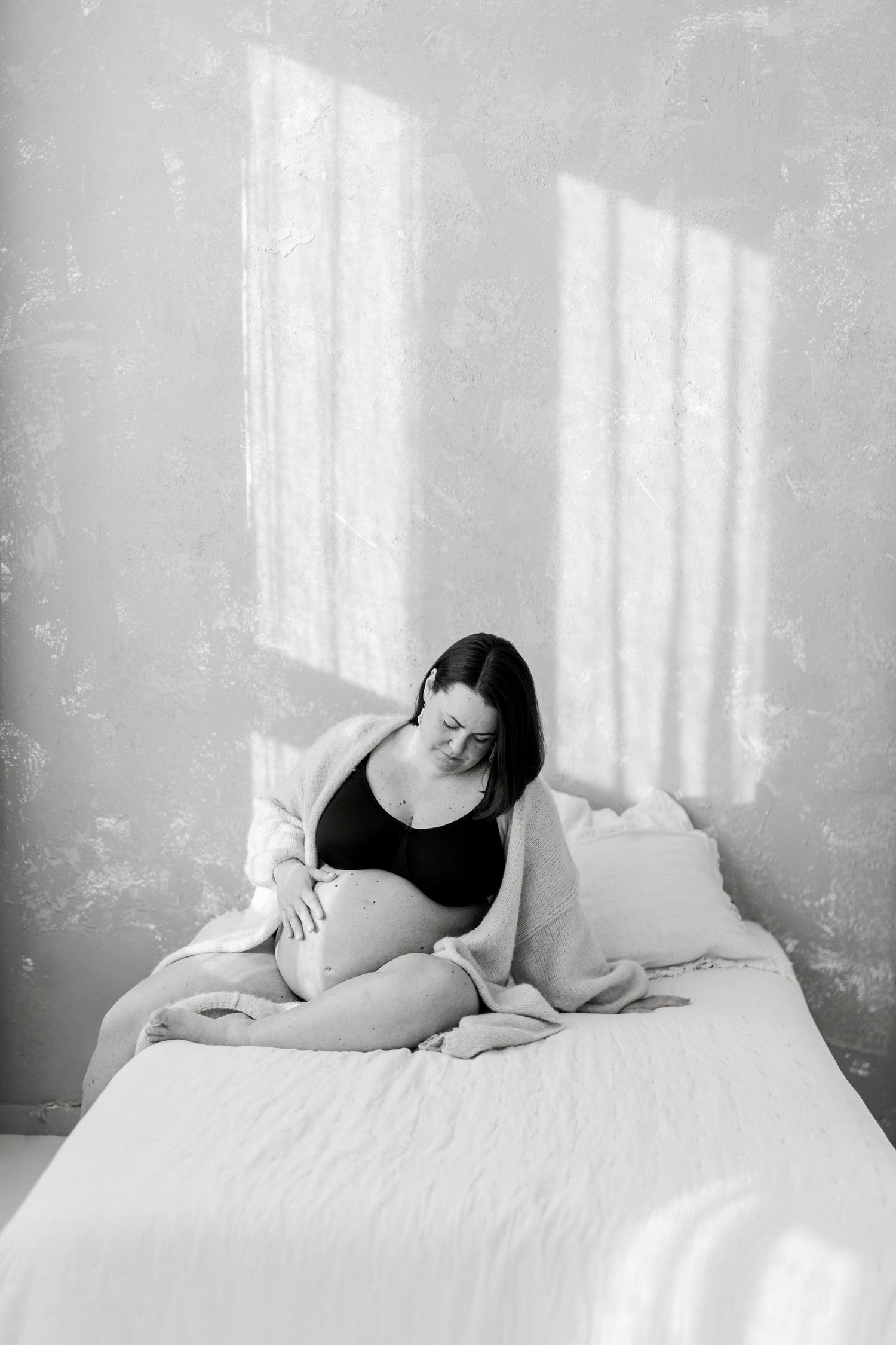A series of black and white photographs showing a person in a dark top reclining on white bedding near a window.