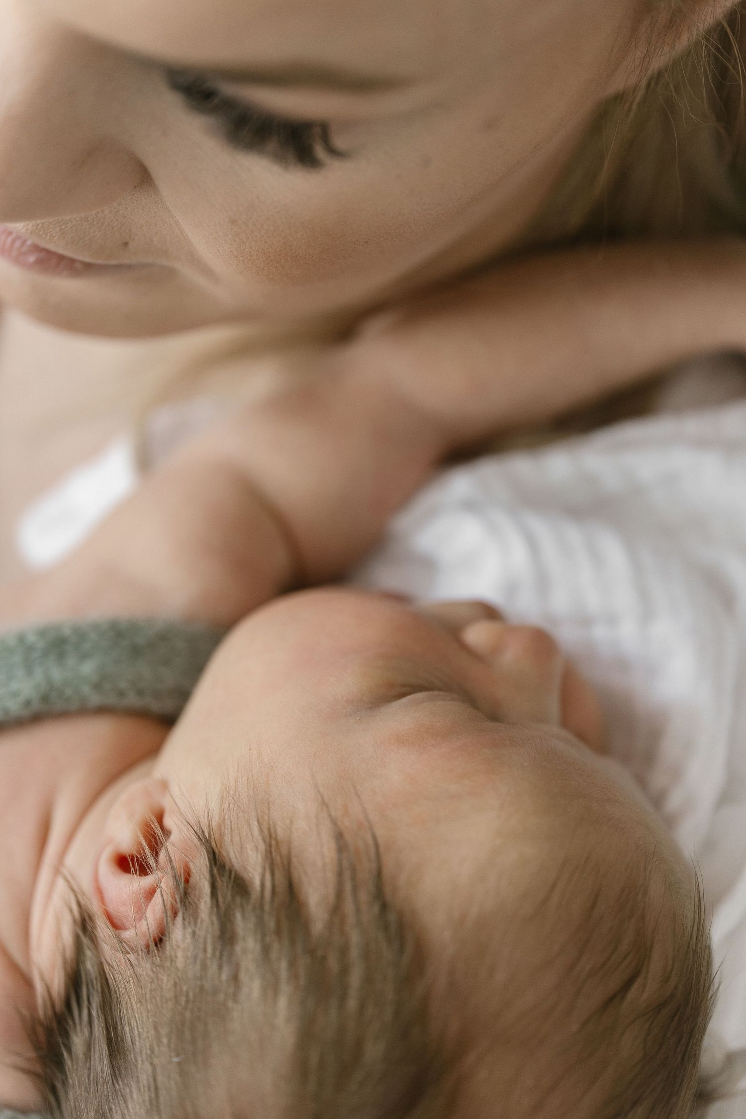 Tender moment between parent and infant lying on white bedding.