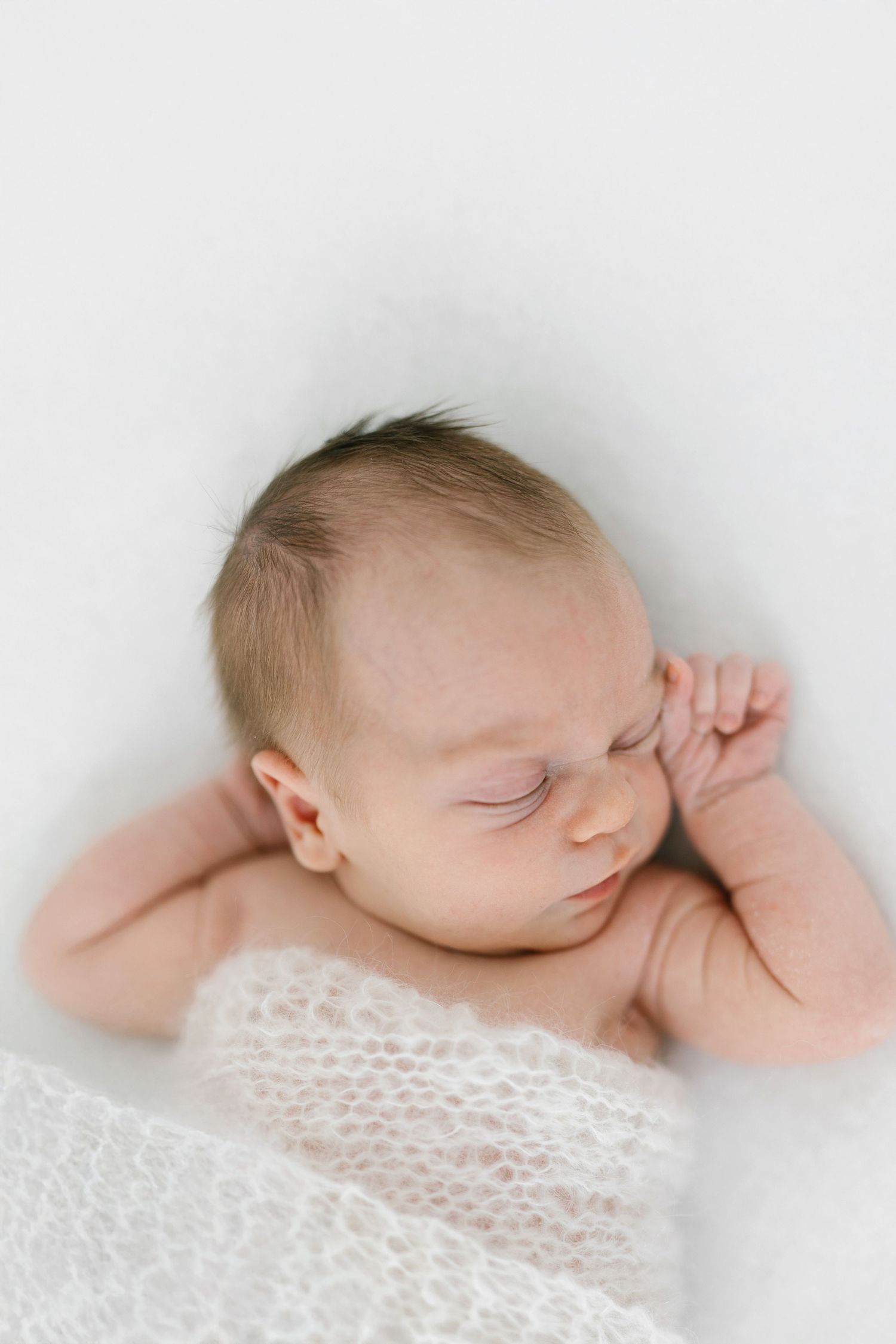 Peaceful newborn baby sleeping wrapped in white lace blanket, soft natural light photography.