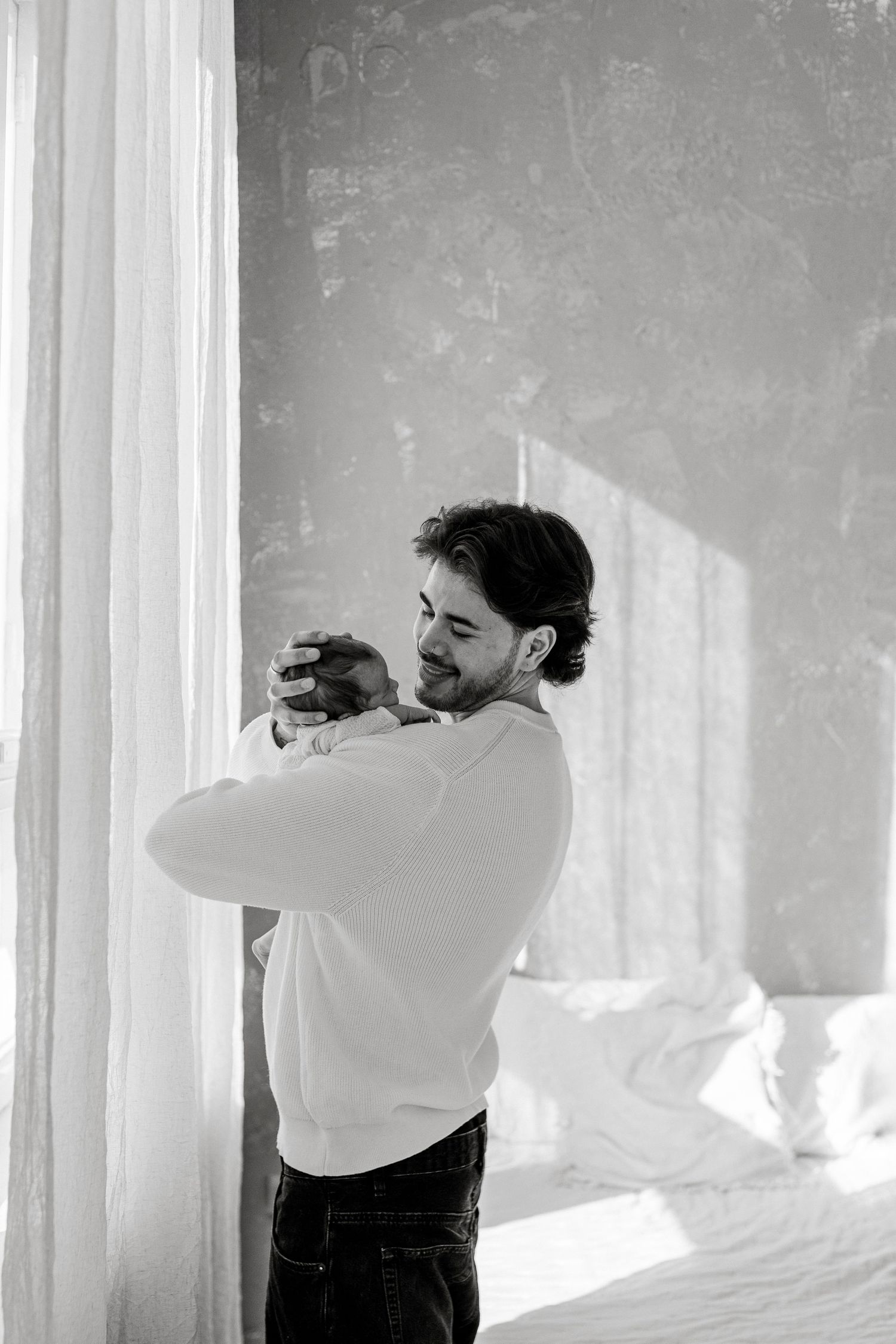 A photographer in a white sweater and jeans takes photos near a bright window in black and white.