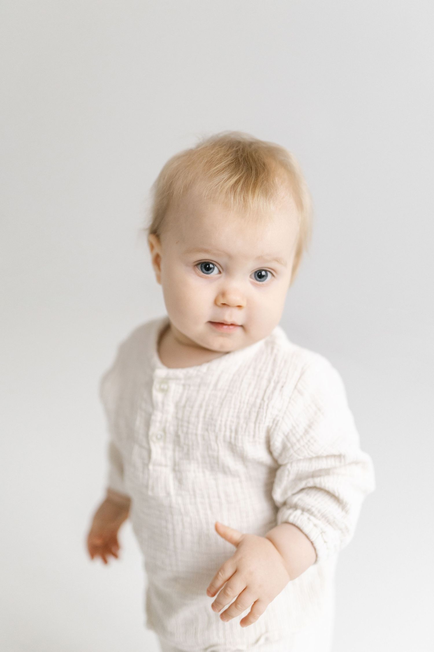 Infant in cream colored outfit against white background showing different expressions.