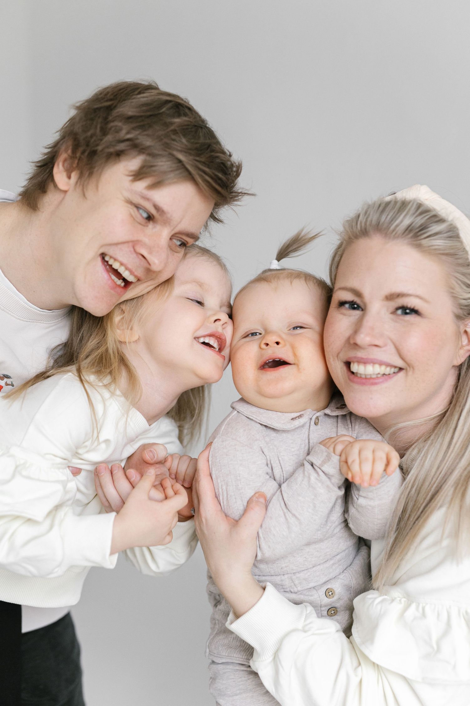 A happy family of four shares joyful laughter together against a white backdrop.