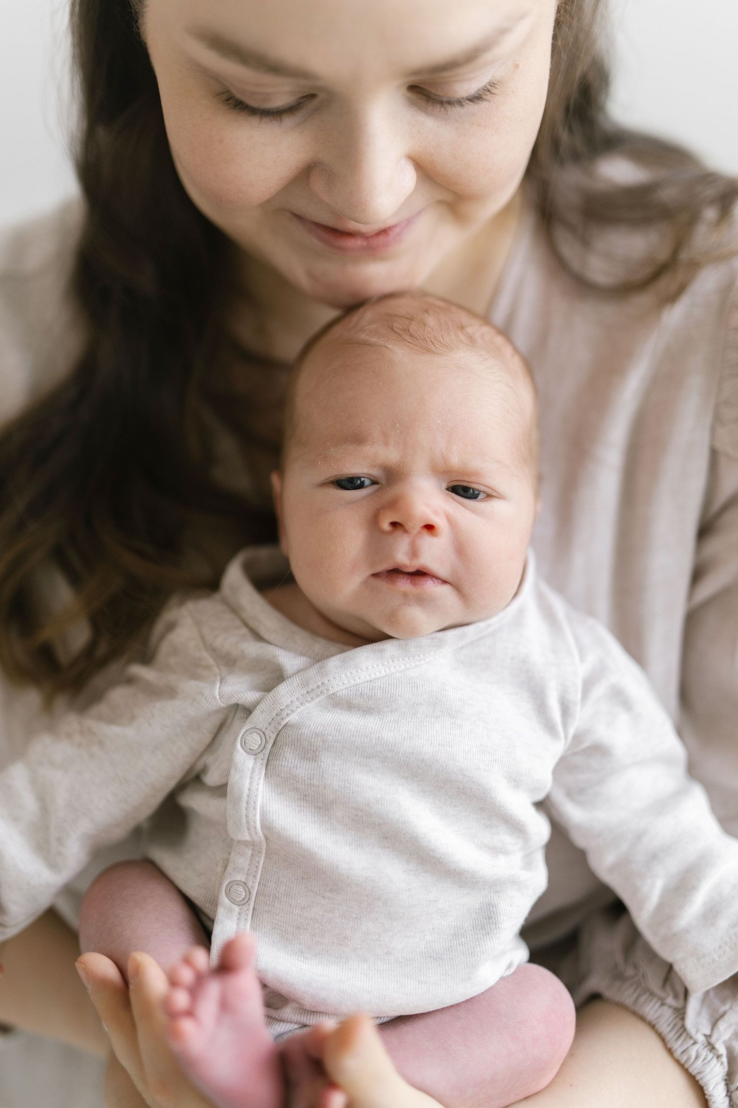 Newborn in white onesie looking up while being held.