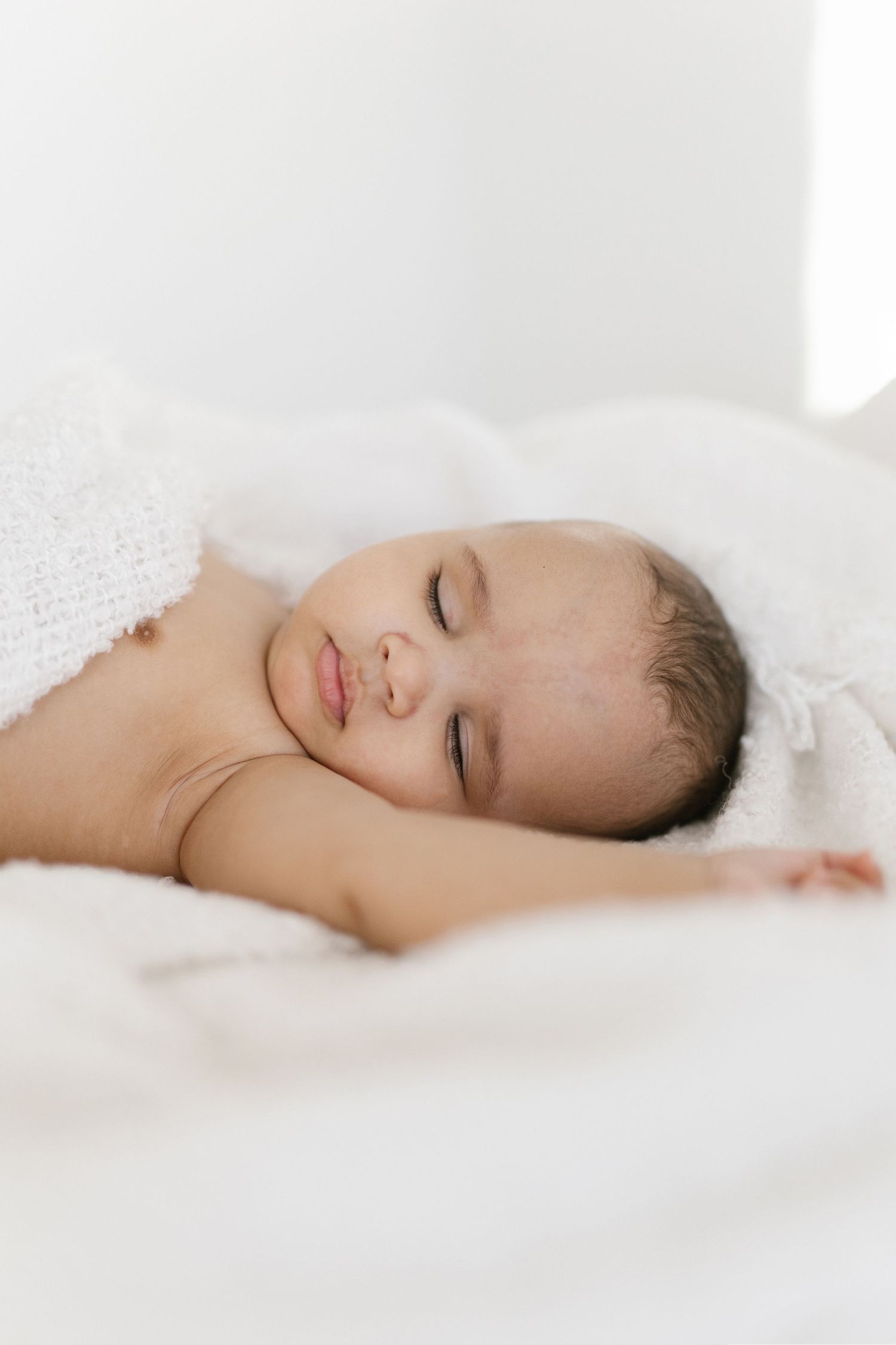 A peaceful newborn baby sleeping soundly on soft white blankets, wrapped in a cozy white knit blanket.