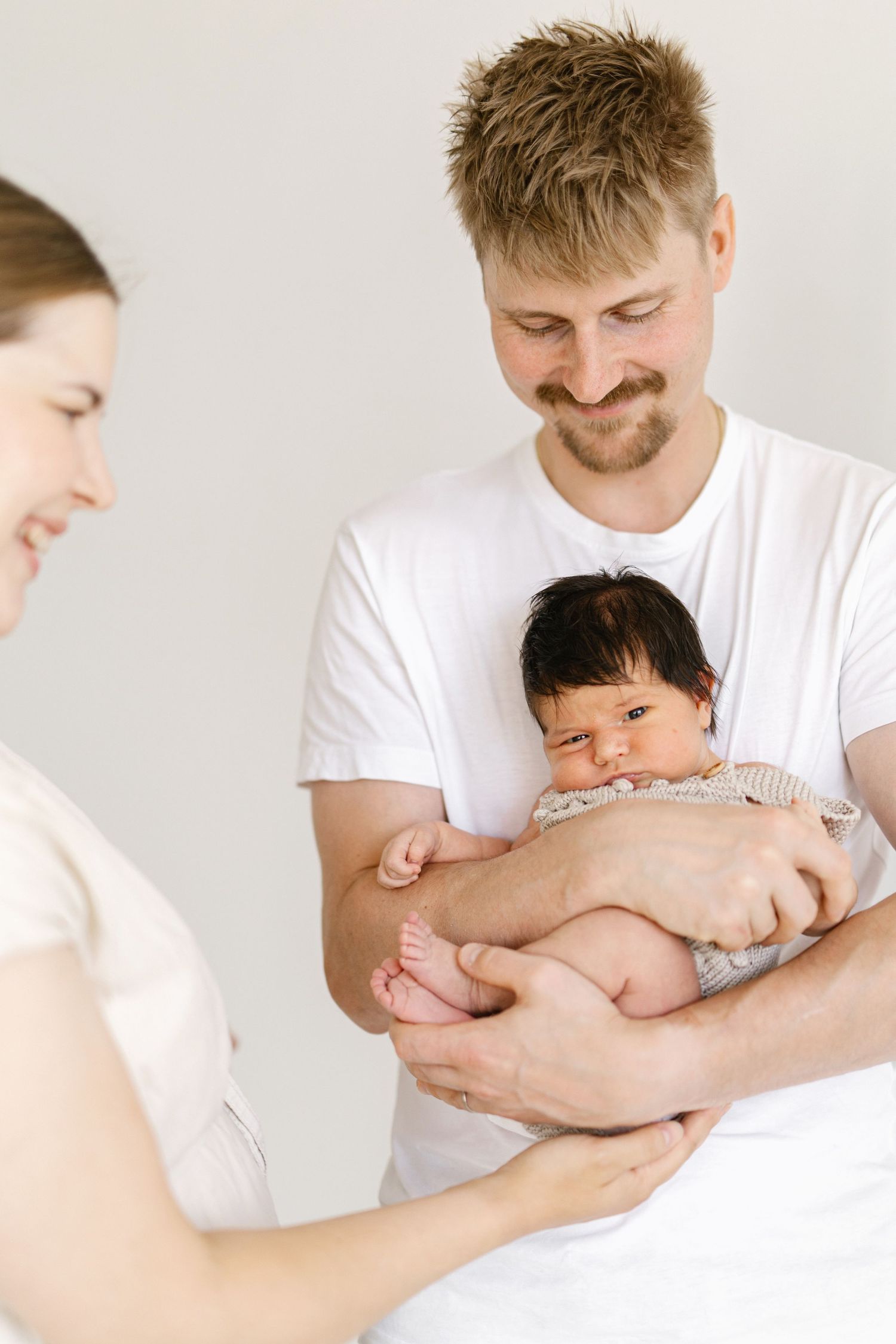 Happy parents holding their newborn baby, smiling lovingly in a bright, minimalist setting.