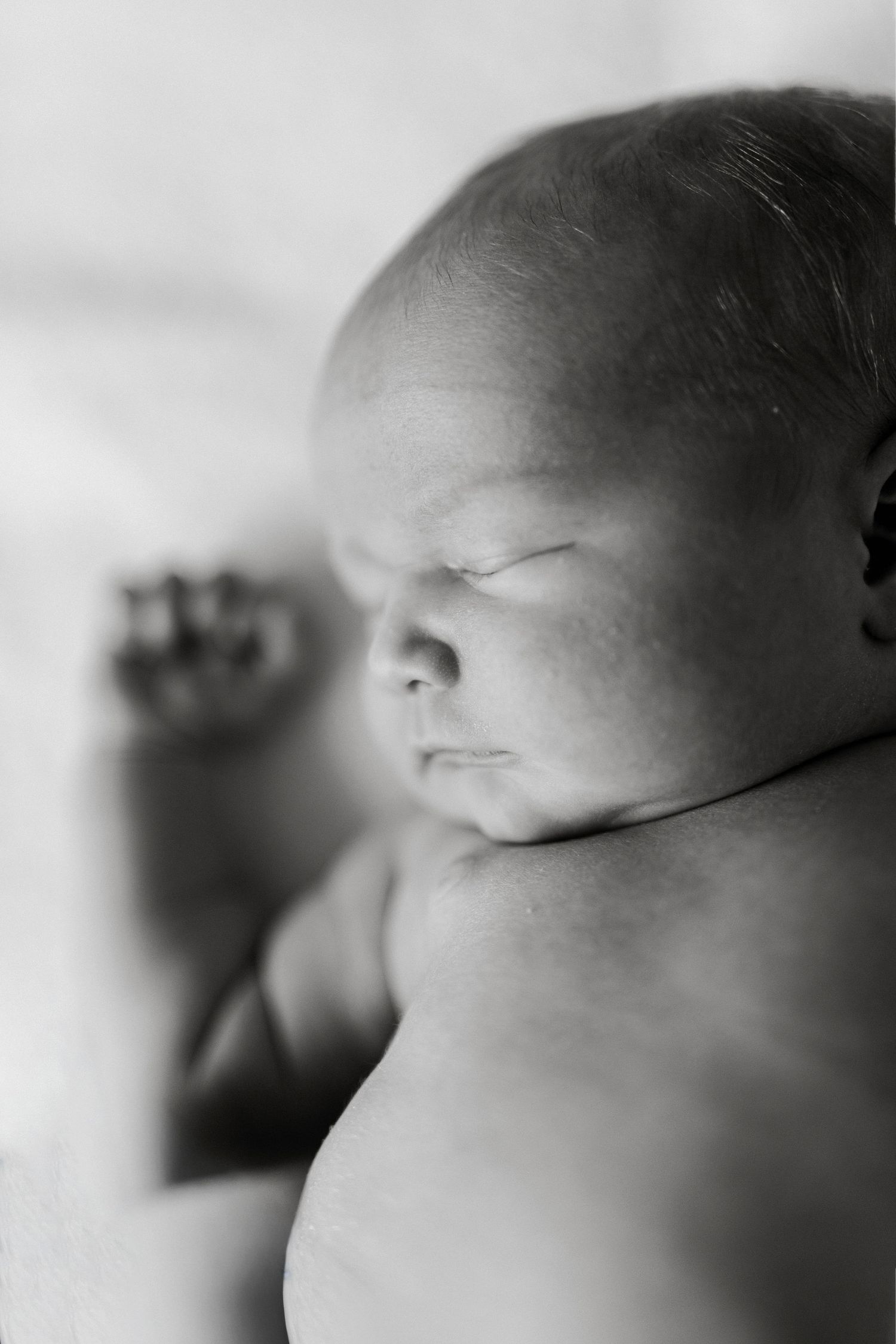Black and white close-up photo of a peaceful sleeping newborn baby with tiny fist visible.
