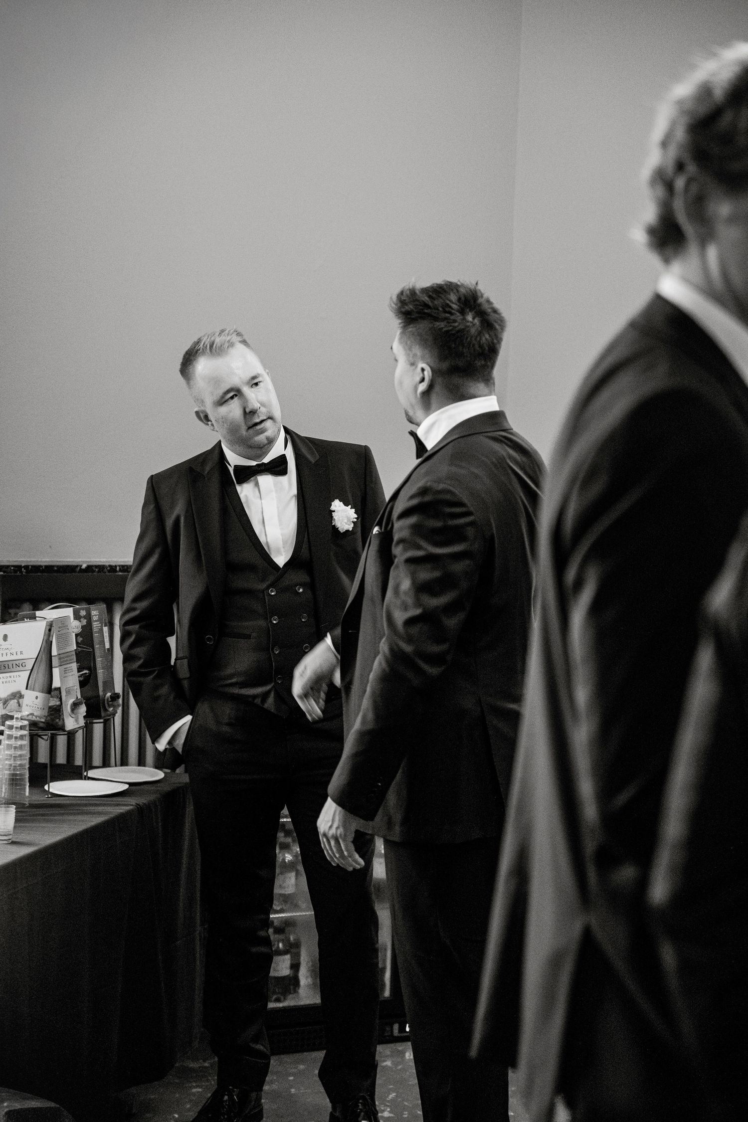 Groomsmen in formal black suits sharing a candid moment before the ceremony.