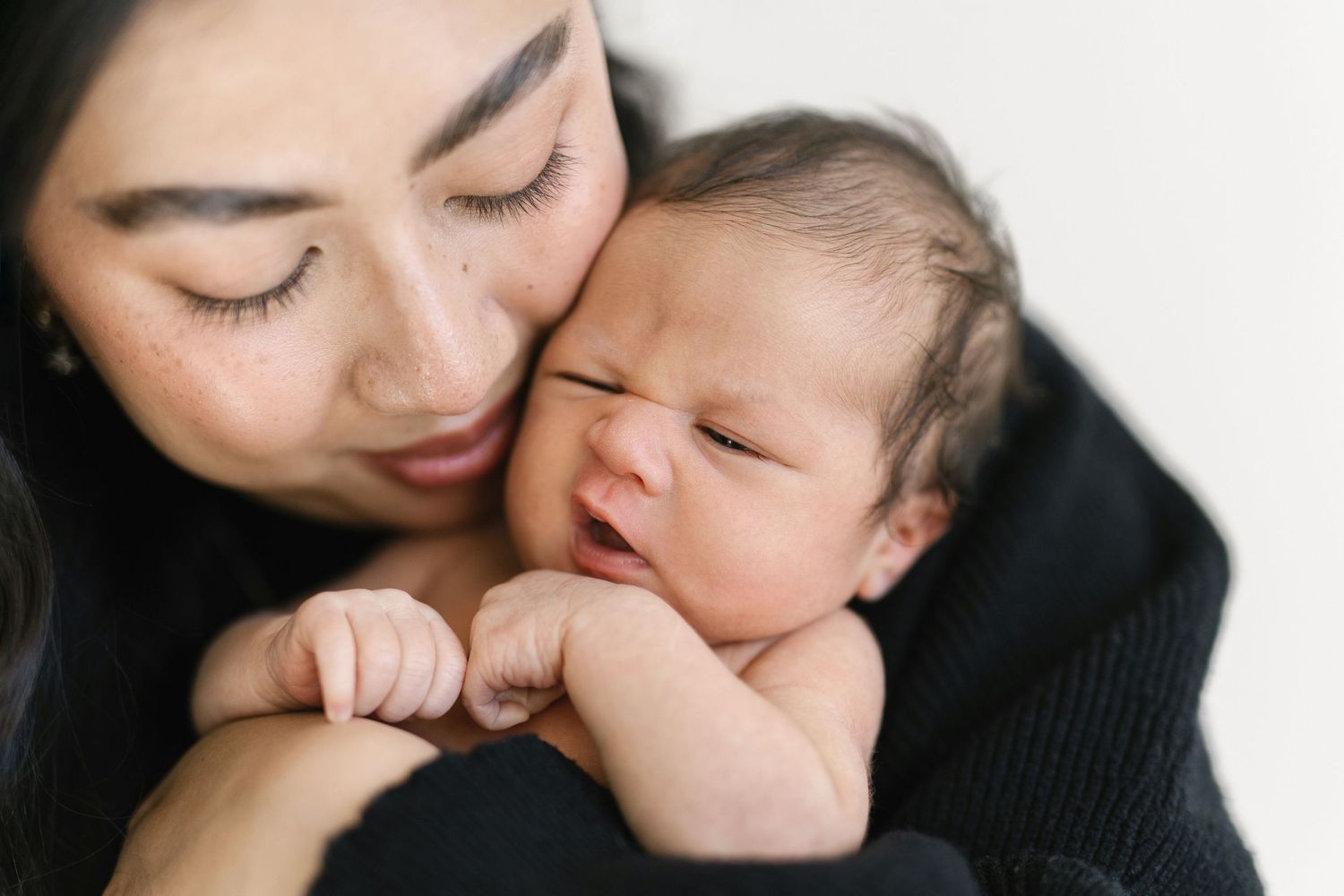 A mother tenderly holds her newborn baby close, gently pressing her cheek against the infant's head.
