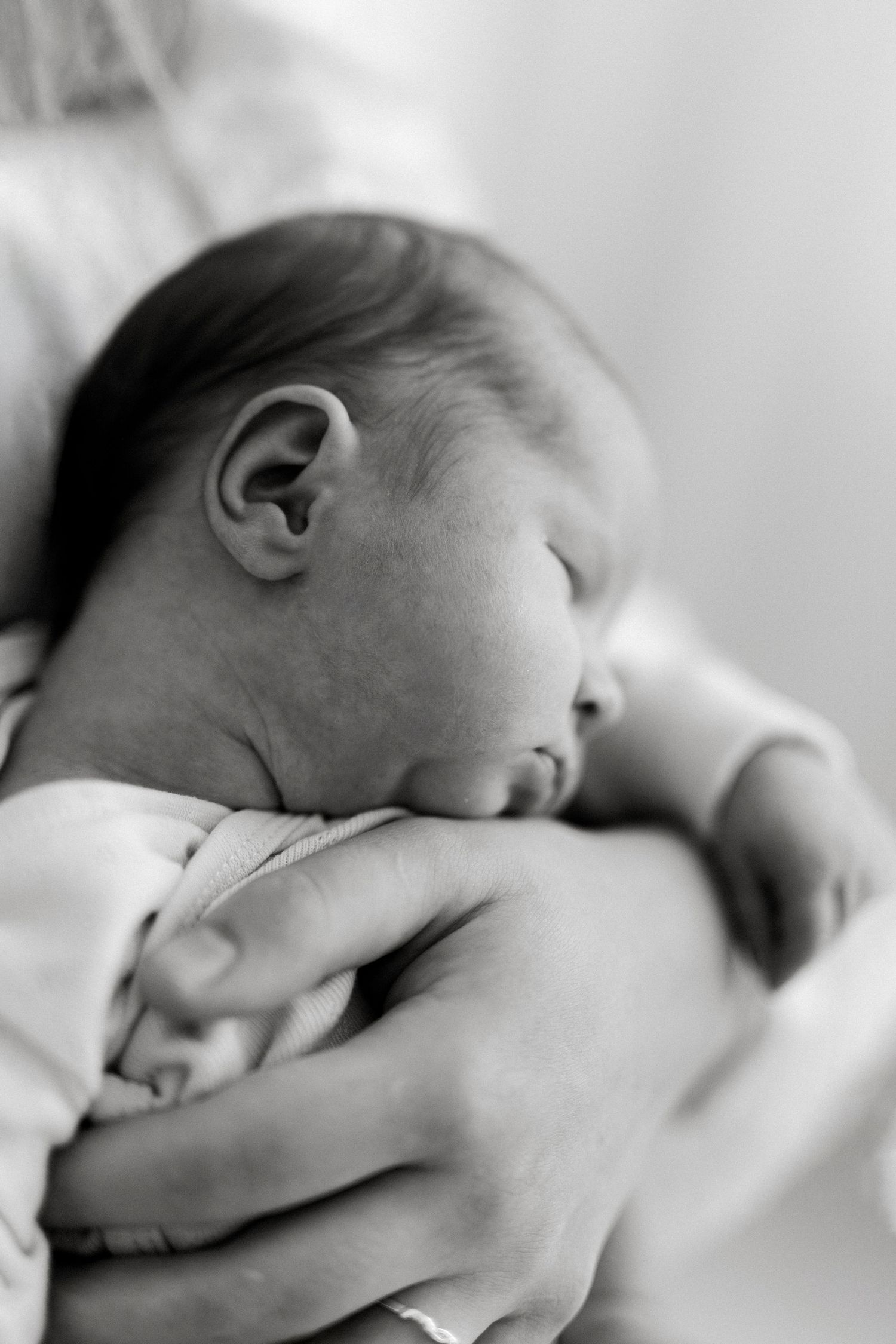 Black and white photo of a sleeping newborn baby cradled gently in an adult's hands.