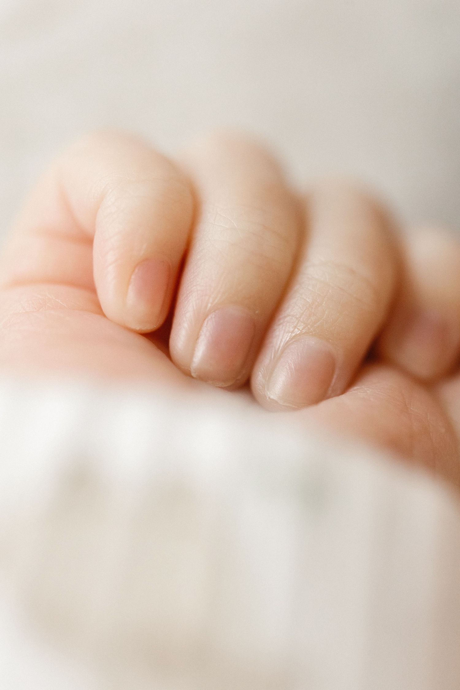 Close-up of a baby's tiny hand with delicate fingers and soft pink nails resting on a white surface.