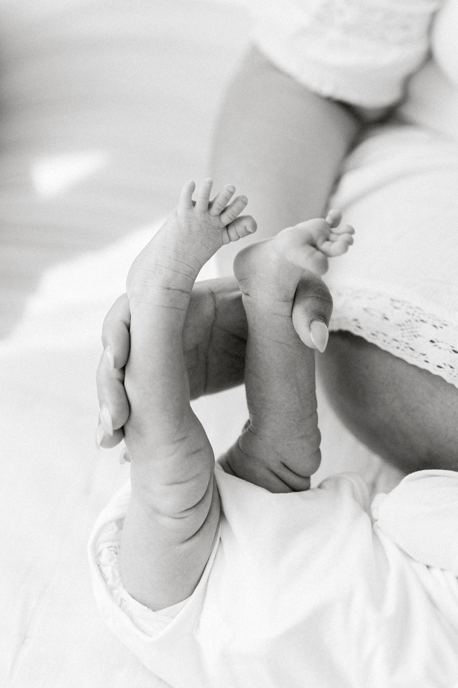 Black and white photo of a parent gently holding a newborn baby's tiny feet and legs.