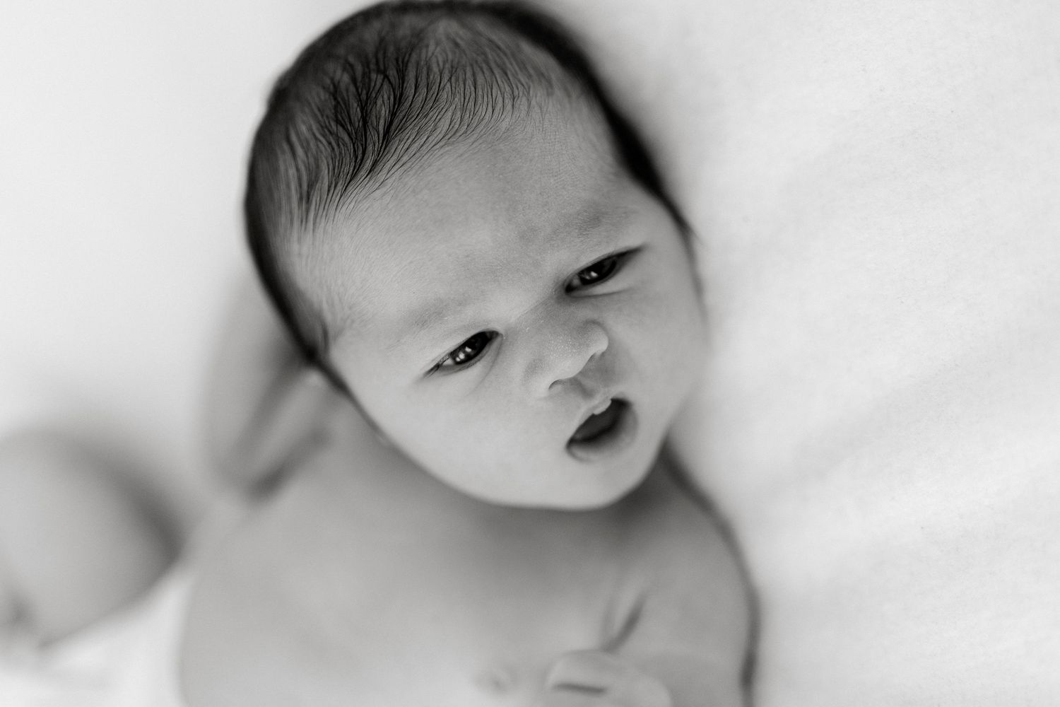 Black and white newborn baby portrait with soft focus, infant gazing upward with delicate features.