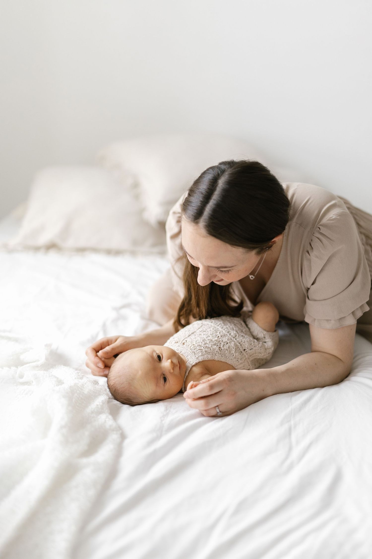 Tender moment between parent and baby lying on white bedding in soft natural light.