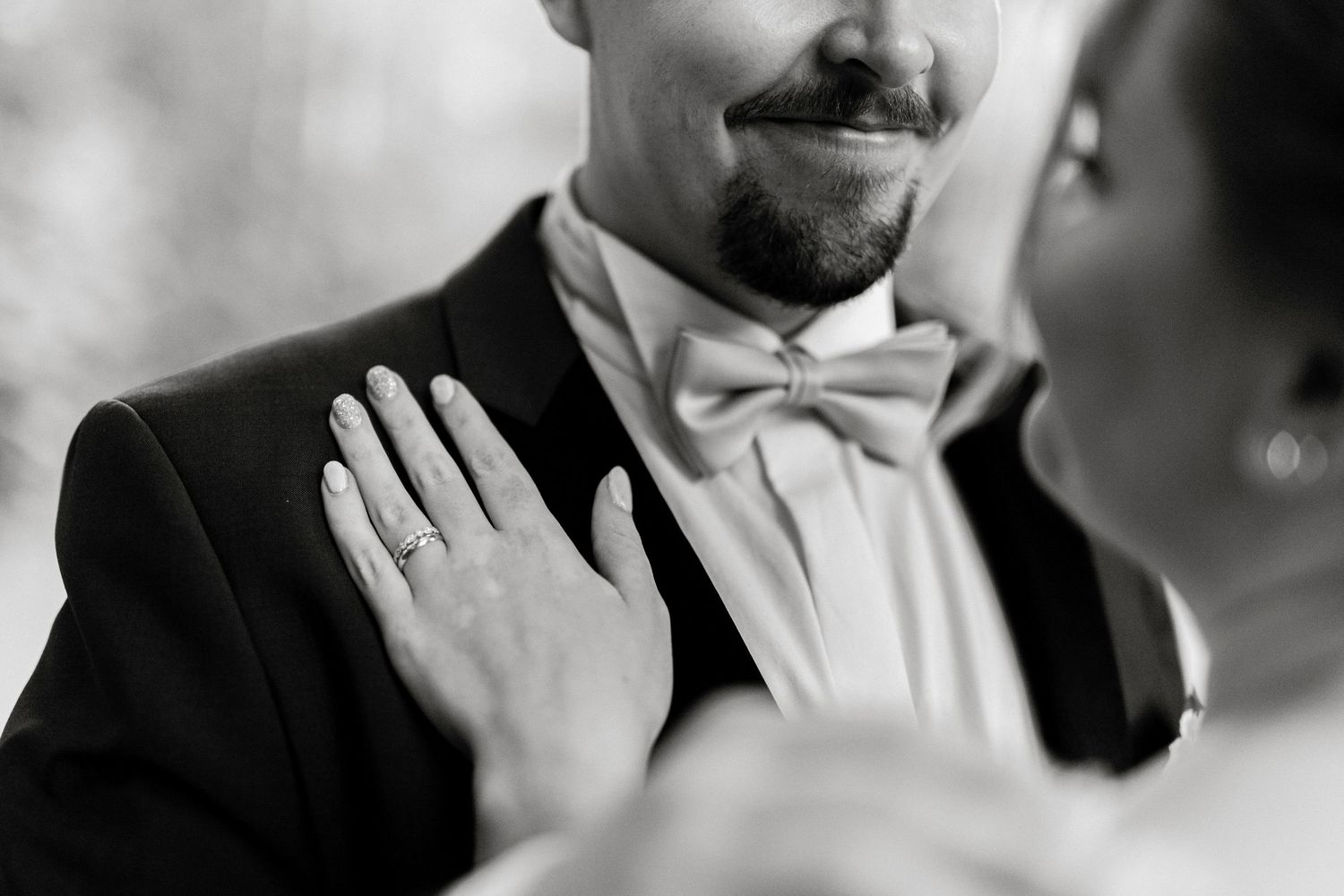 Close-up of groom with bowtie as bride touches his lapel during wedding moment.