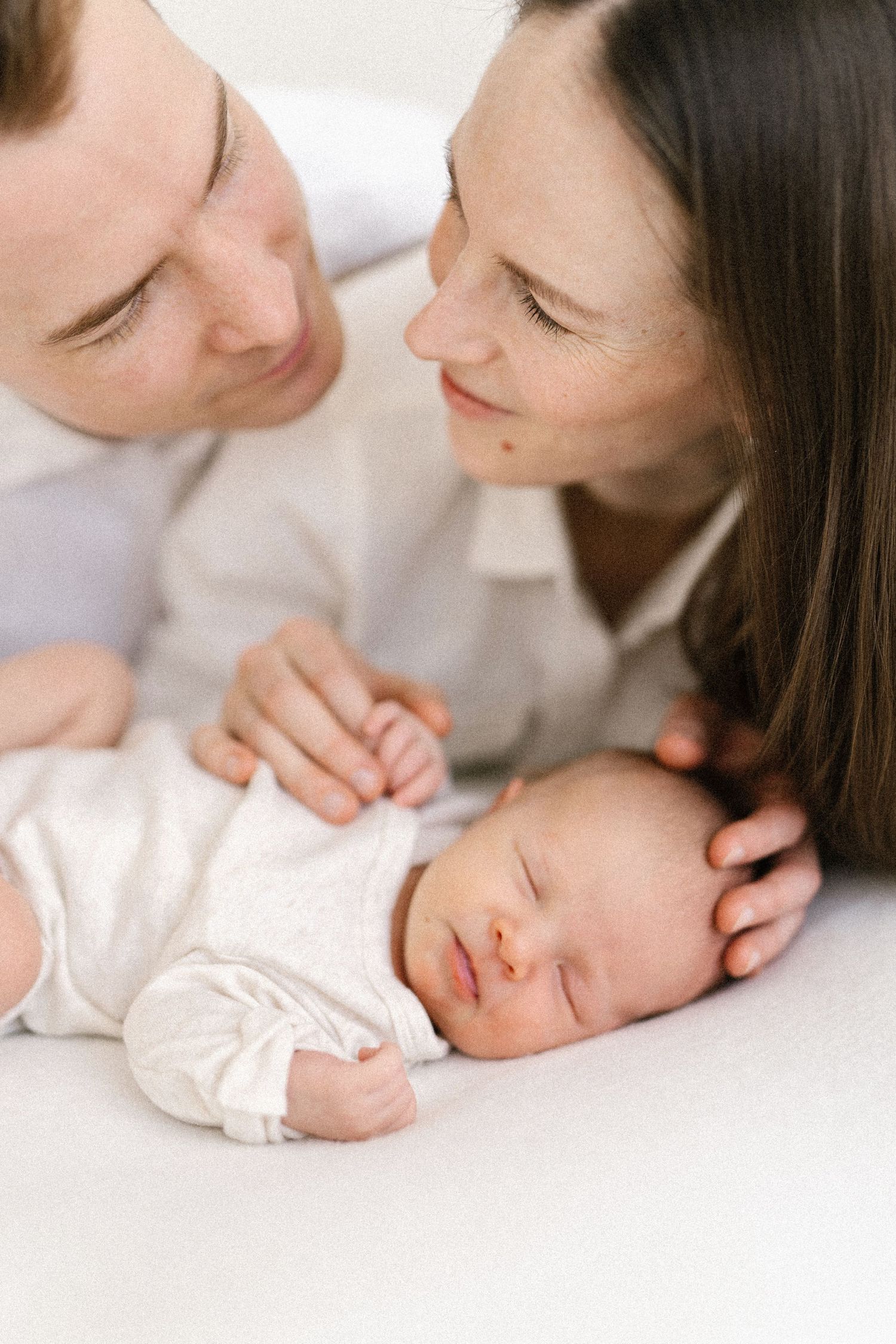 Series of tender moments between parent and newborn baby in minimalist white setting.